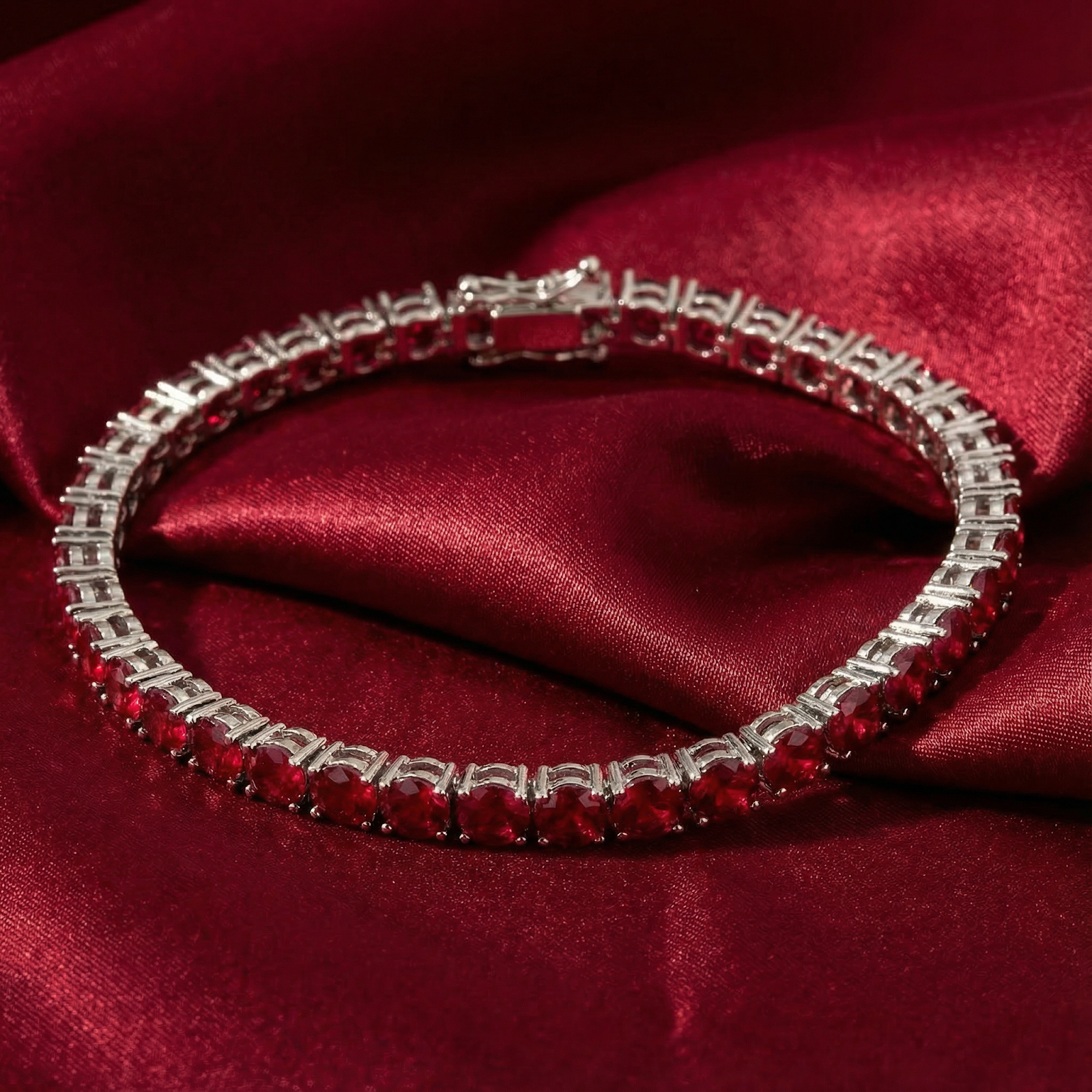 Silver-toned tennis bracelet with round red gemstones resting on draped red satin.