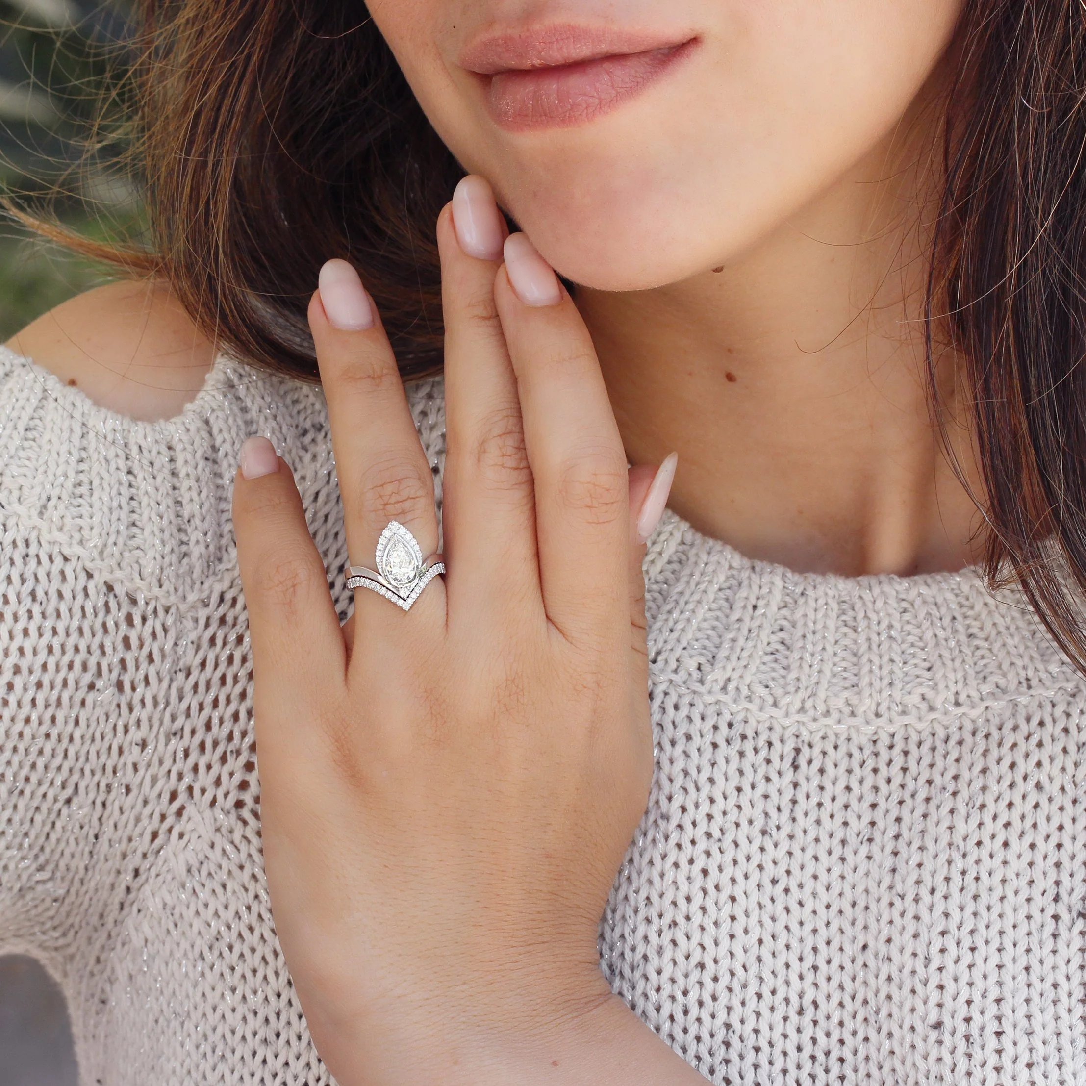 Close-up of a hand near a mouth showing a silver-toned stacked ring set with a pear-shaped gem.