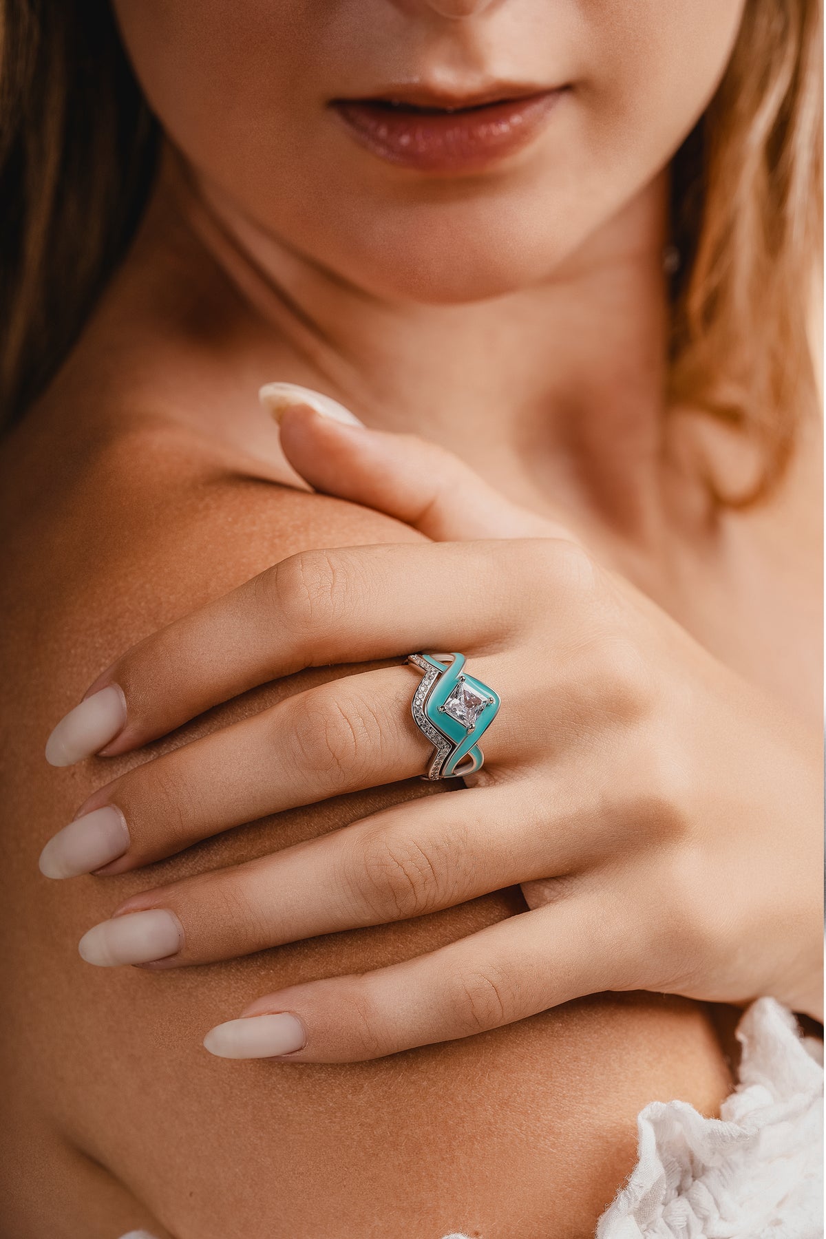 A woman rests her hand on her shoulder, wearing a silver-toned ring with turquoise accents and a clear square stone.