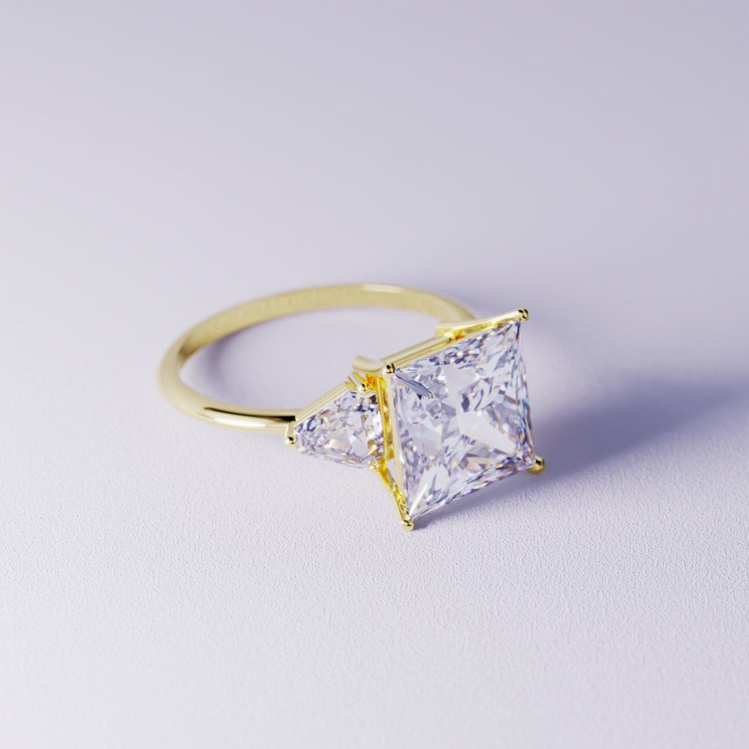 Gold-toned ring with a large square clear centerpiece and two triangular side accents on a light purple surface.