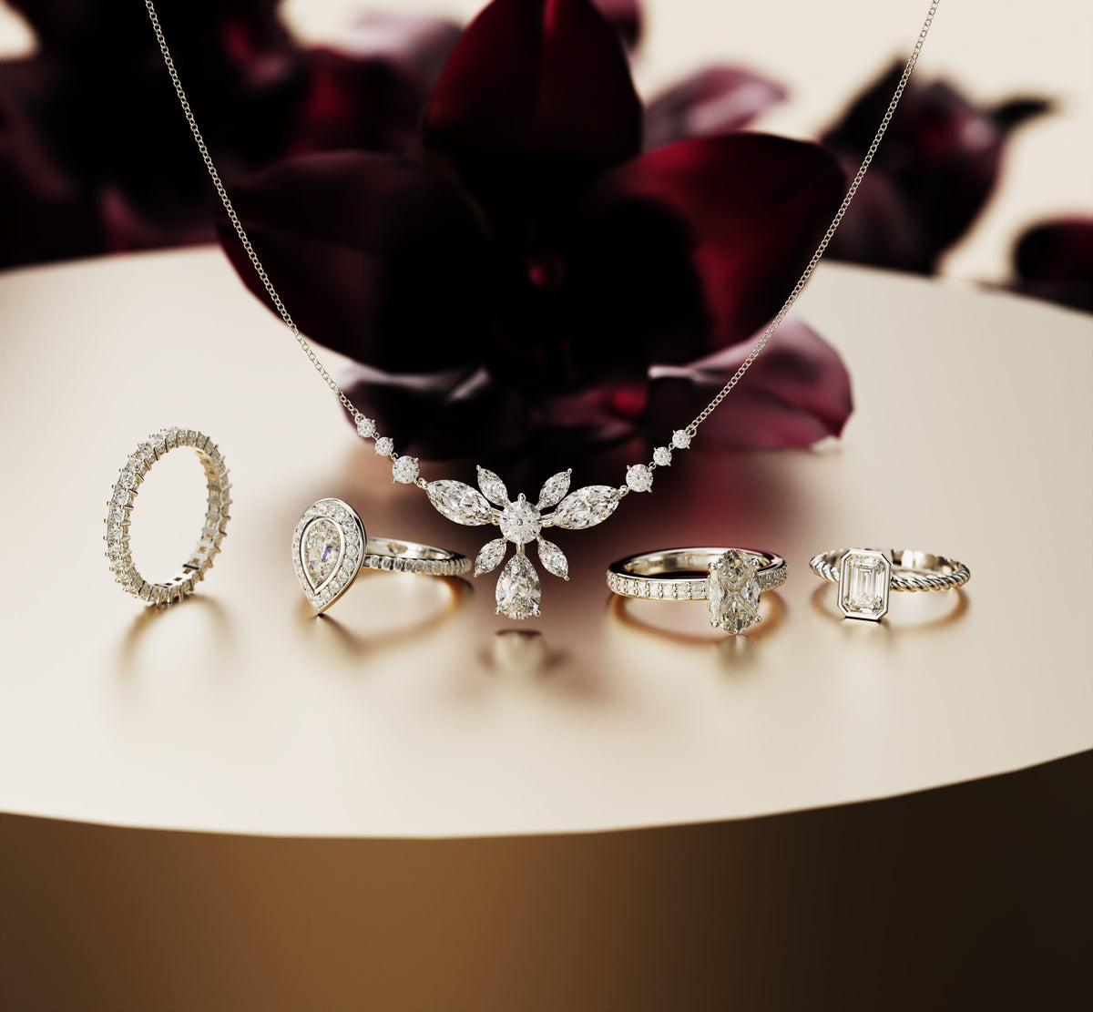 Silver-toned gemstone rings and a floral pendant necklace arranged on a polished gold-toned pedestal.