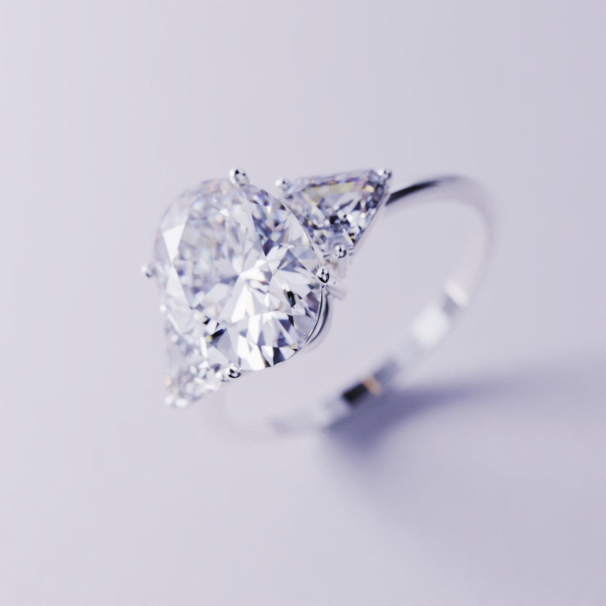 Silver-toned three-stone ring with a large pear-shaped faceted center gem and two triangular side gems.