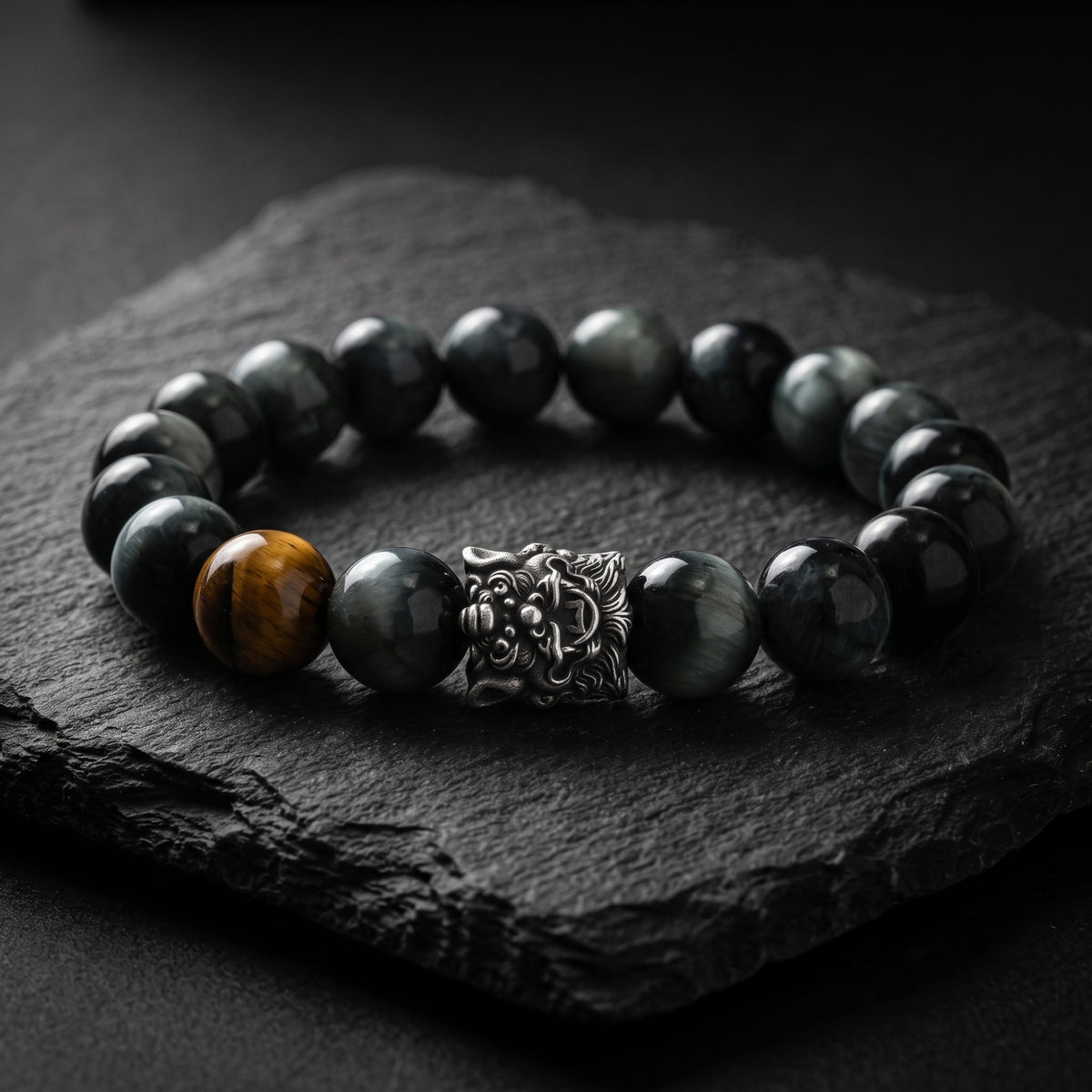 Lion-head silver beaded bracelet with dark eagle eye beads and one brown tiger eye bead on black slate.