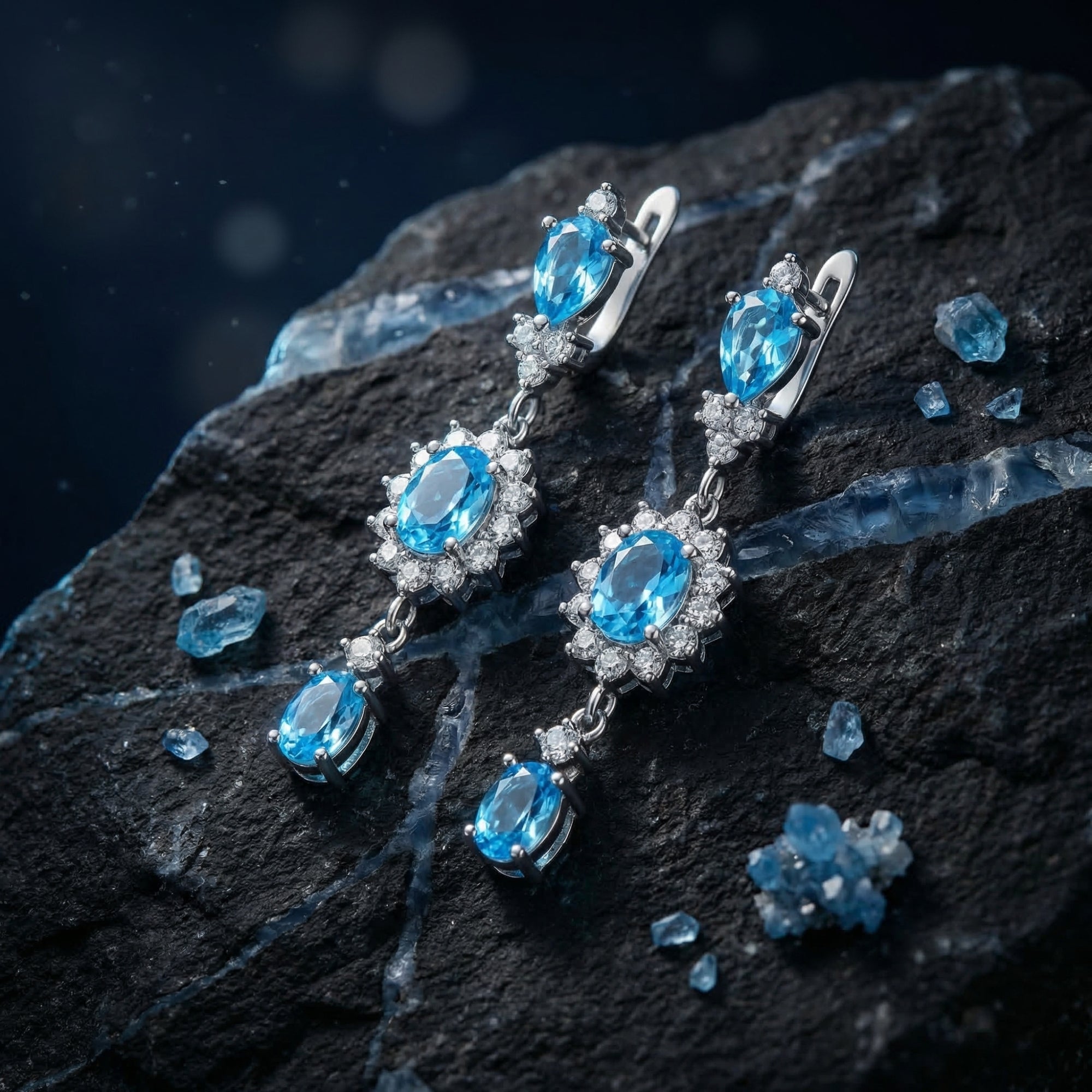 Silver drop earrings with pear and oval Swiss blue topaz stones displayed on a dark textured rock.