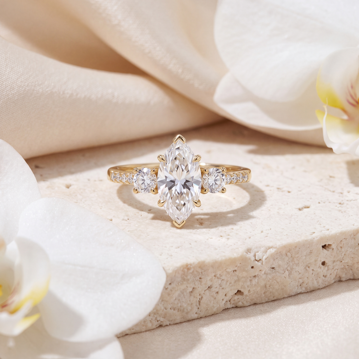 Front view of a marquise cut moissanite three-stone ring set in yellow gold on a beige stone surface.