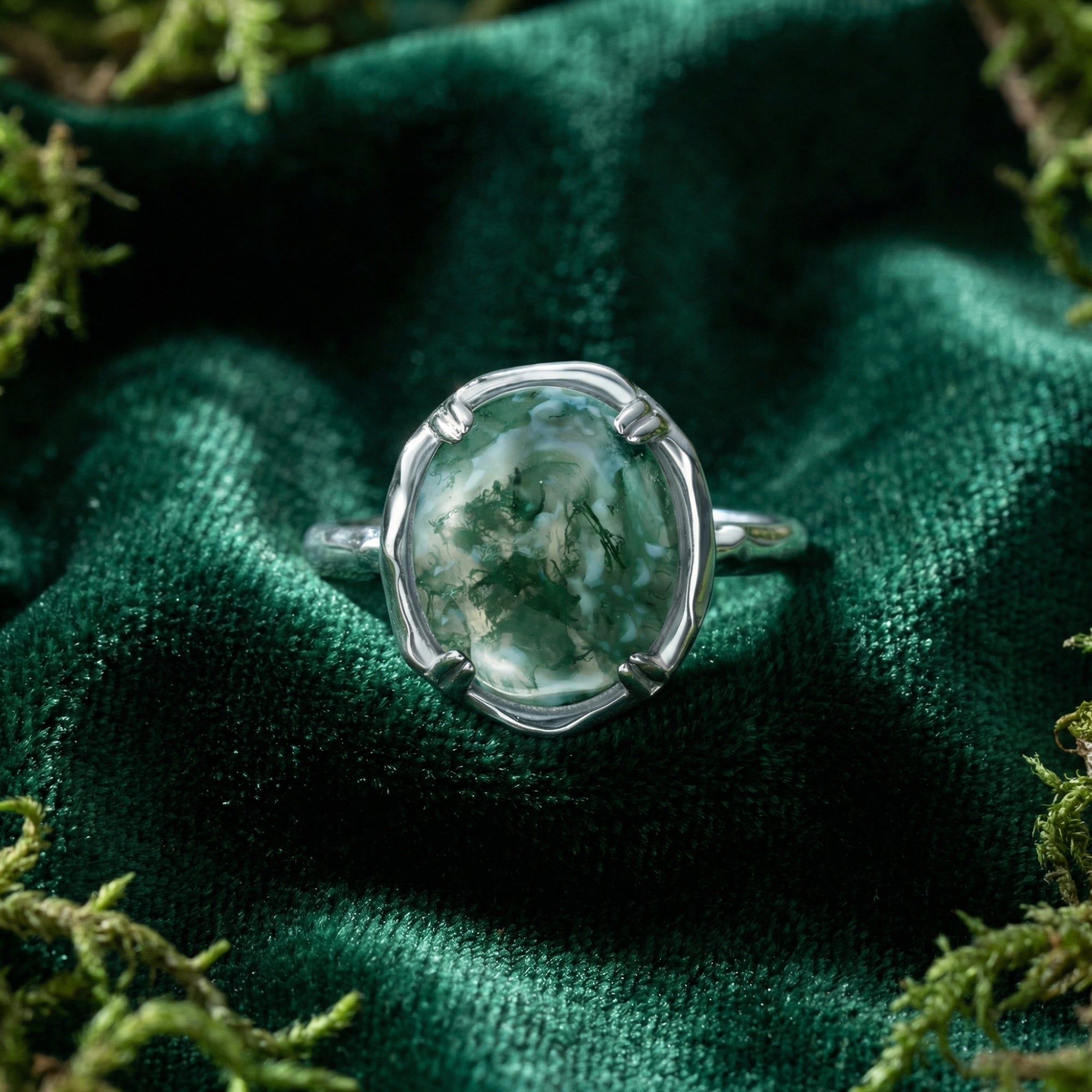 Organic flow sterling silver ring with a round moss agate cabochon on green velvet and natural moss.