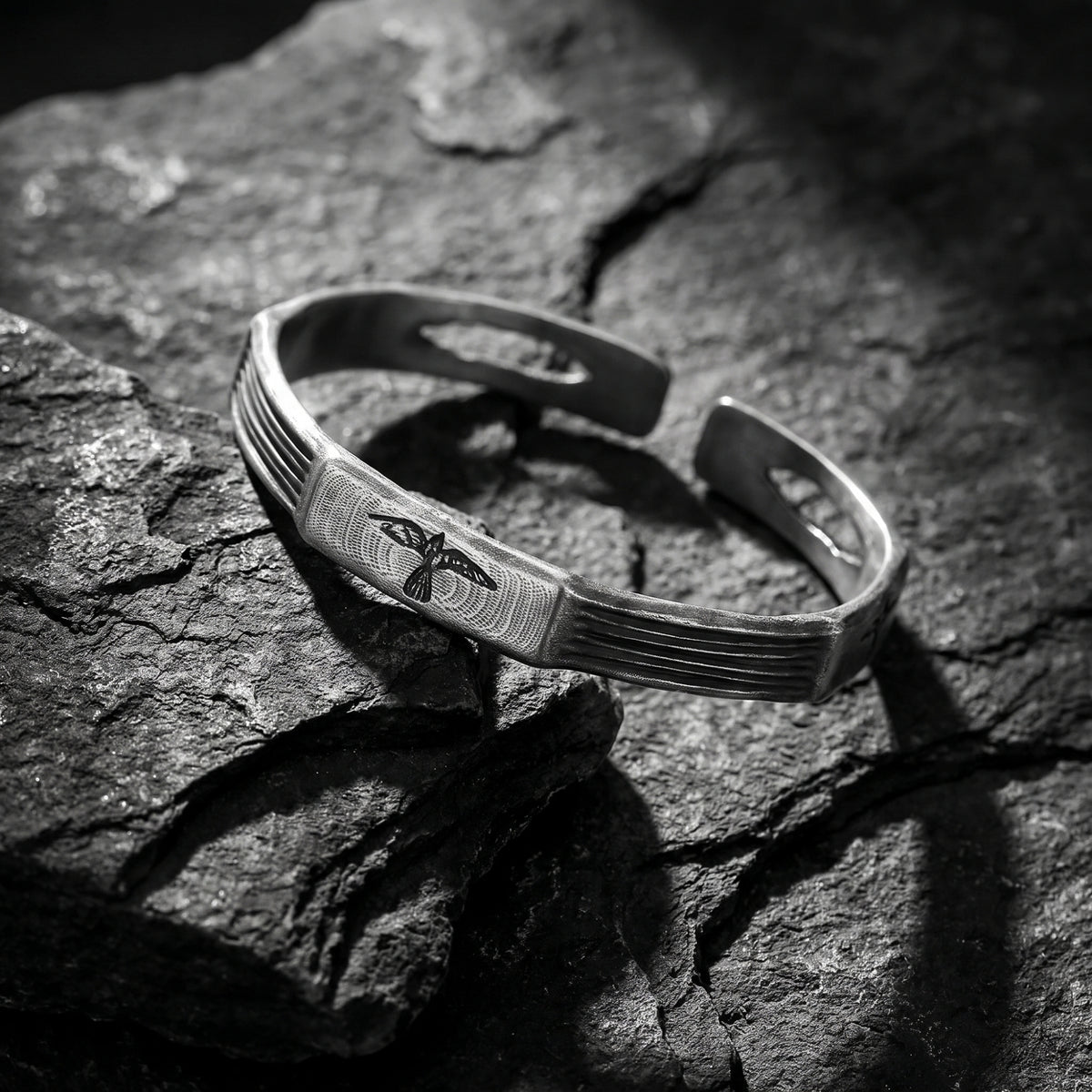Angled view of the silver grooved raven cuff bracelet resting on textured dark slate.