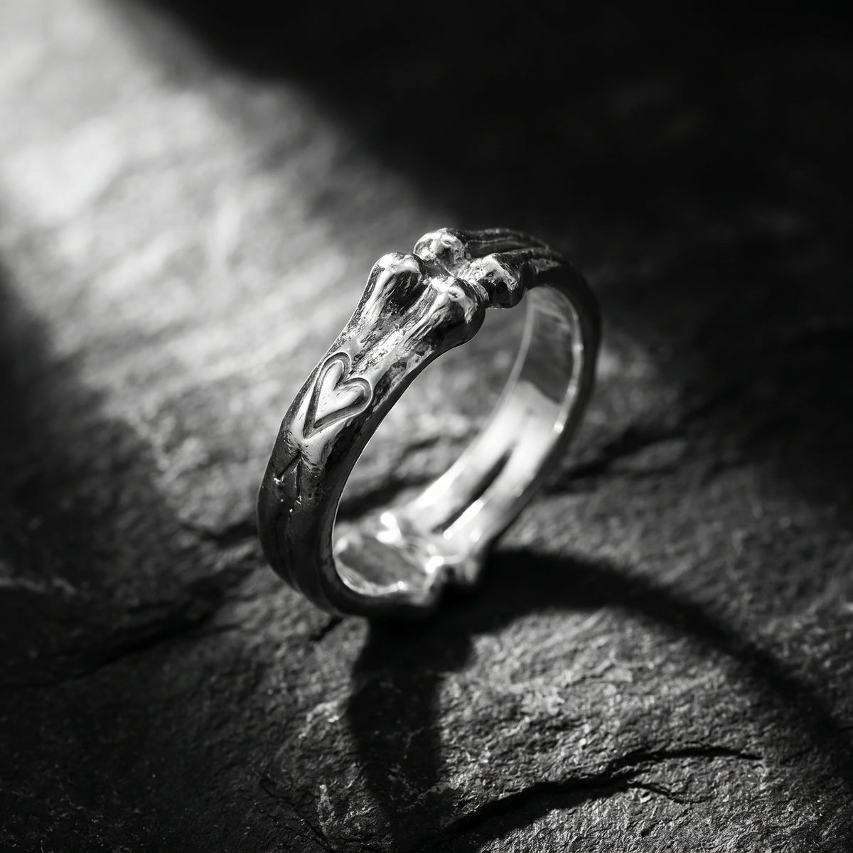 Silver open band ring with a sculpted bone motif and heart detail, standing on textured dark stone.