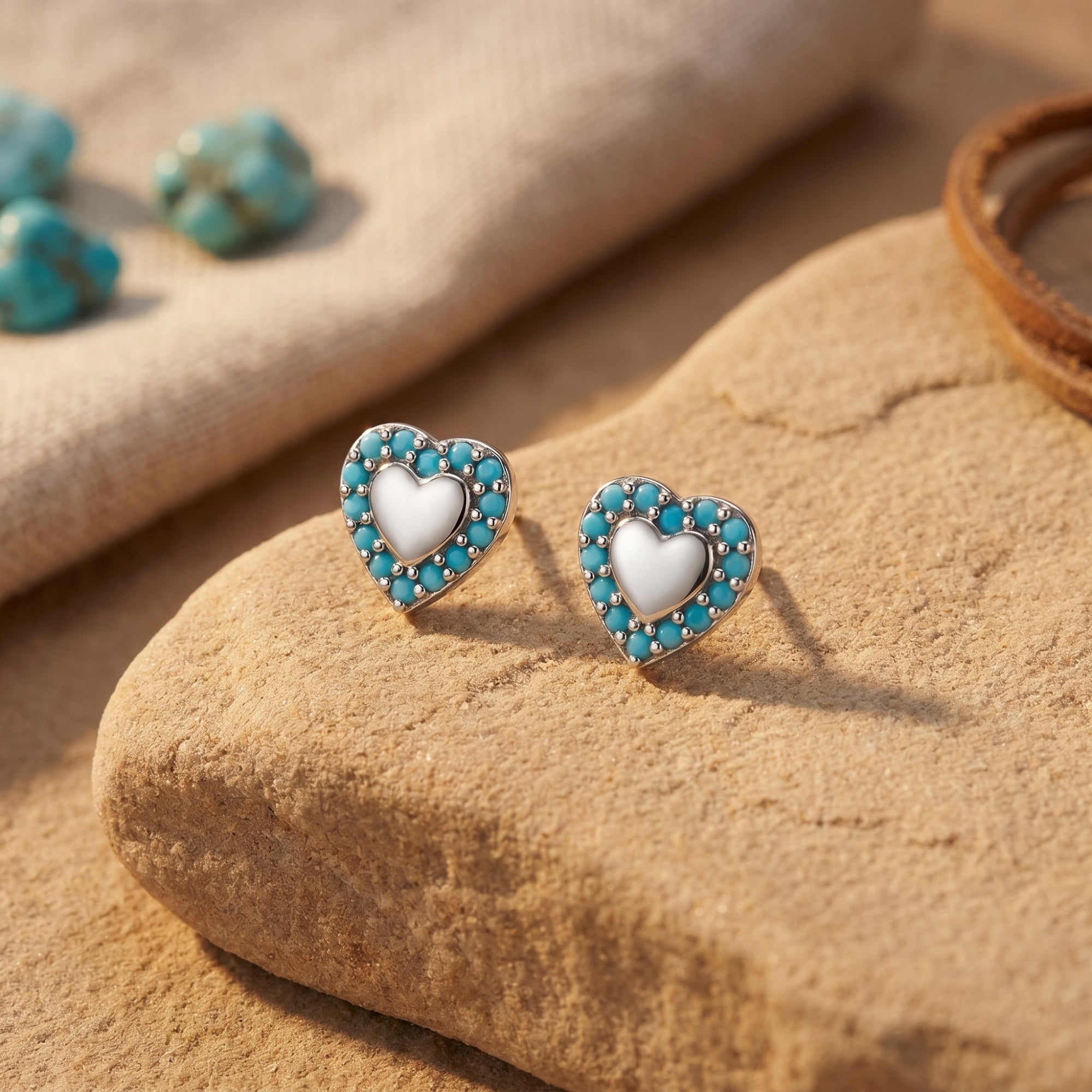 Silver heart stud earrings with turquoise cabochon borders resting on a desert rock in a lifestyle setting.