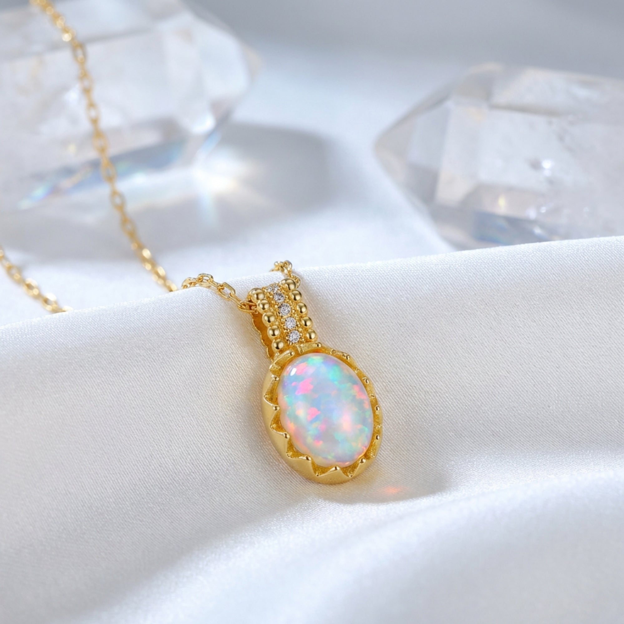 Gold-tone sterling silver necklace with an oval white opal pendant resting on white silk with crystal props.