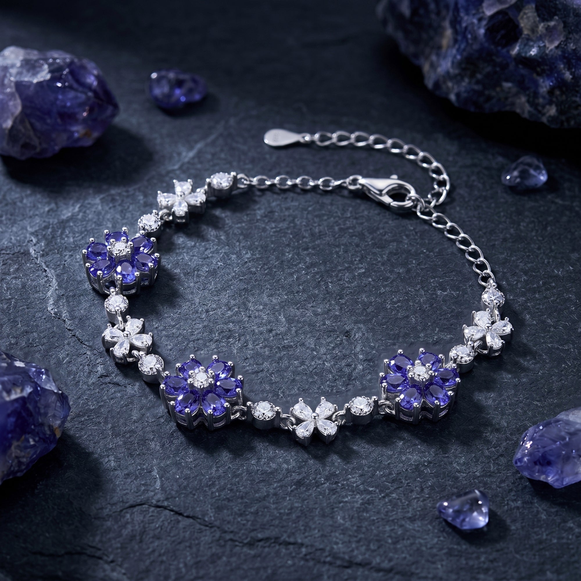 Sterling silver cluster bracelet with pear-cut tanzanite and white stones on a dark textured stone background.