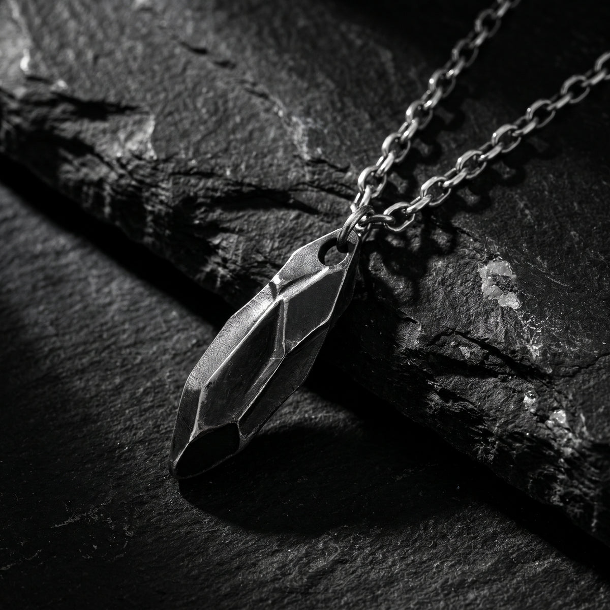 Close-up of a faceted silver shard pendant resting on dark stone.