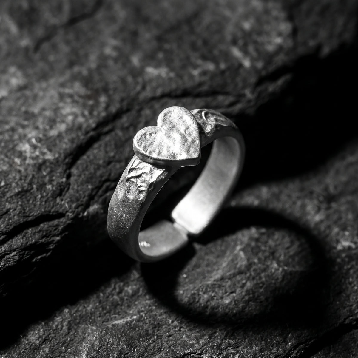 Angled close-up of the hammered heart ring showing its open band on textured rock.