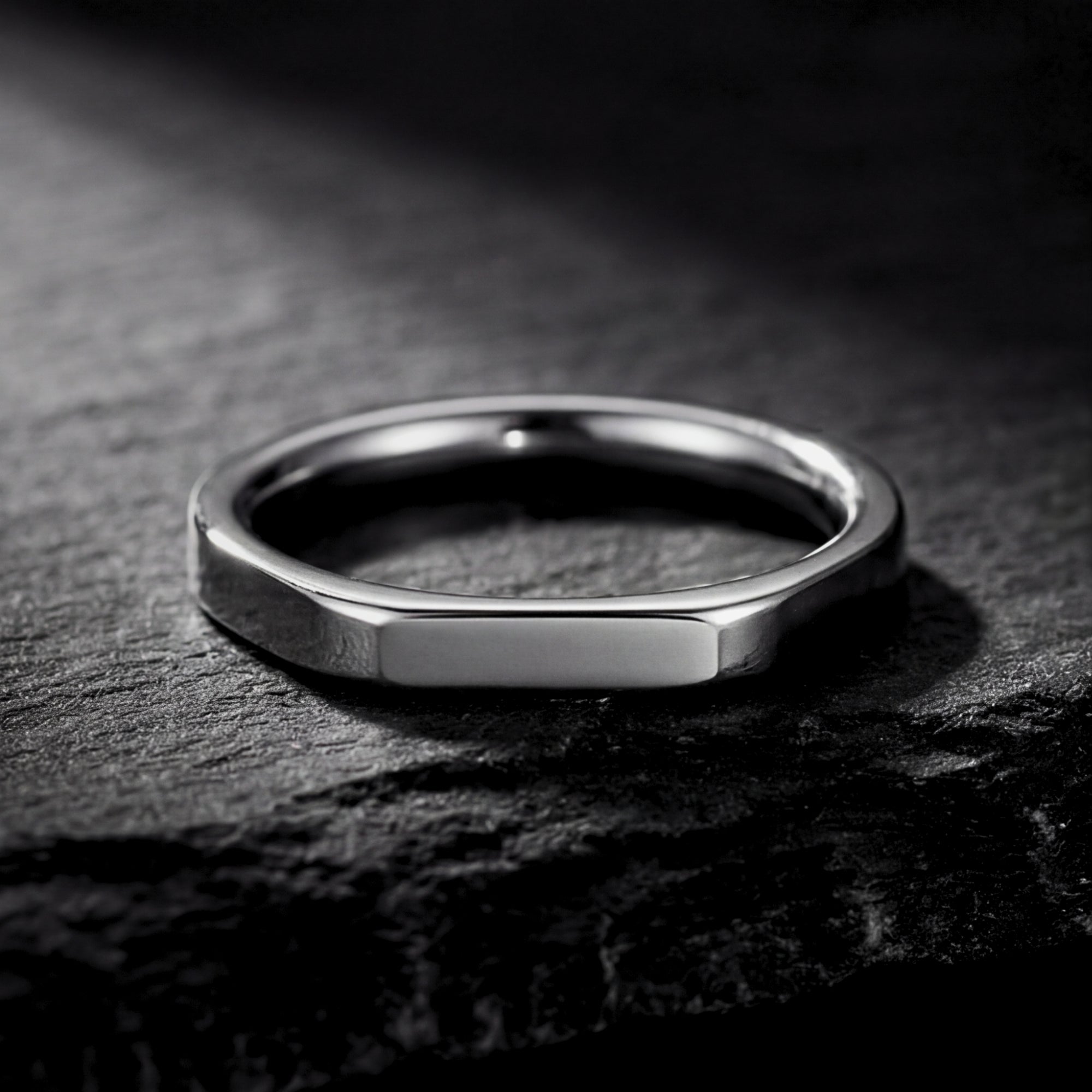 Front view of the minimalist silver stainless steel signet ring lying on a dark slate background.