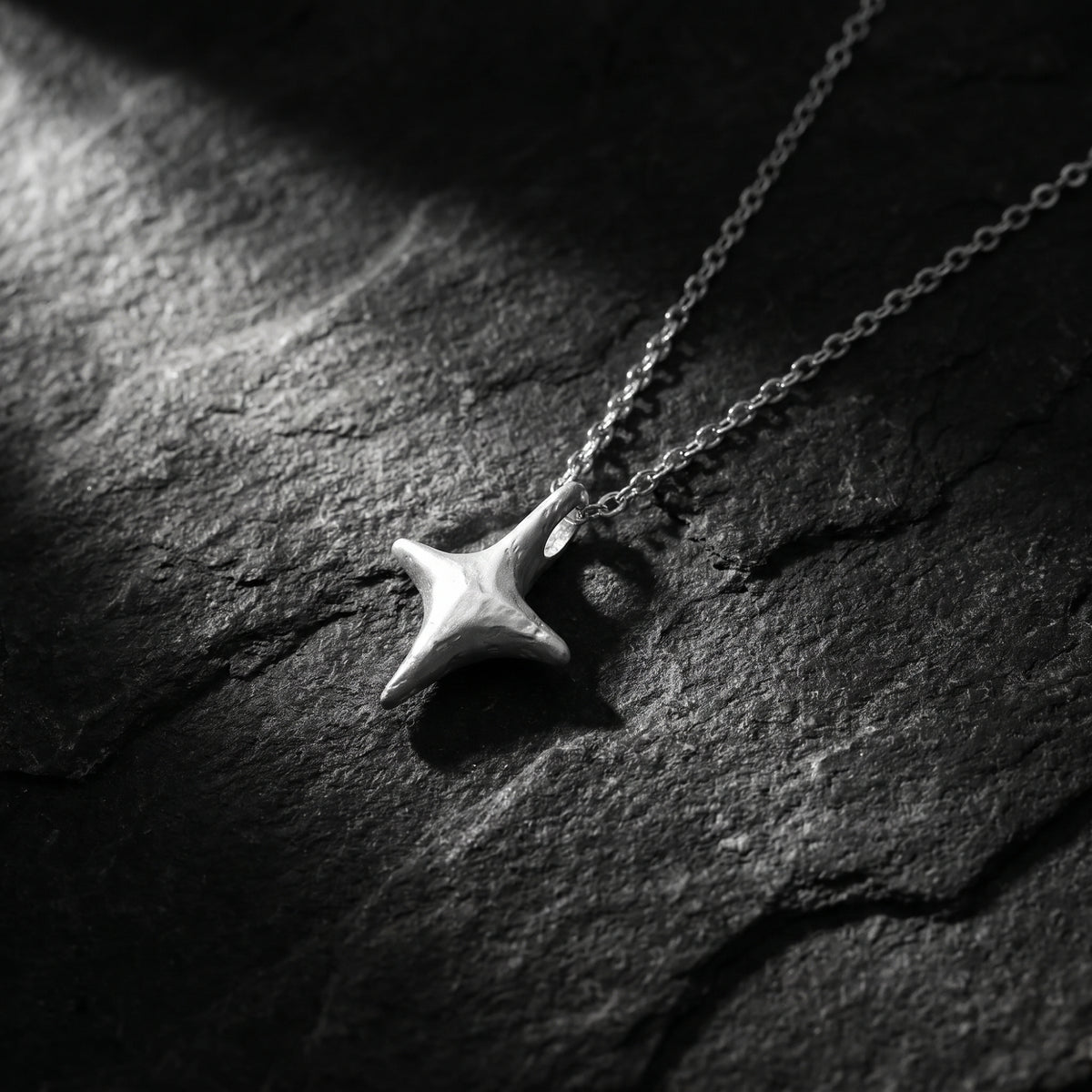 Silver four-point starburst pendant and chain resting on a dark textured surface.