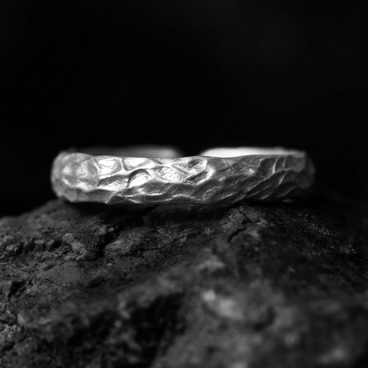 Close-up profile of the silver ring with a carved, weathered surface resting on dark stone.