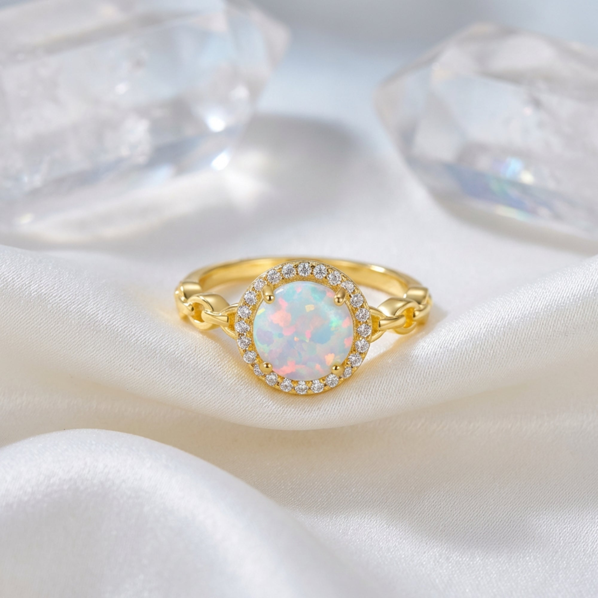 Gold-tone S925 silver statement ring with a round natural white opal and halo, styled on white silk with crystals.