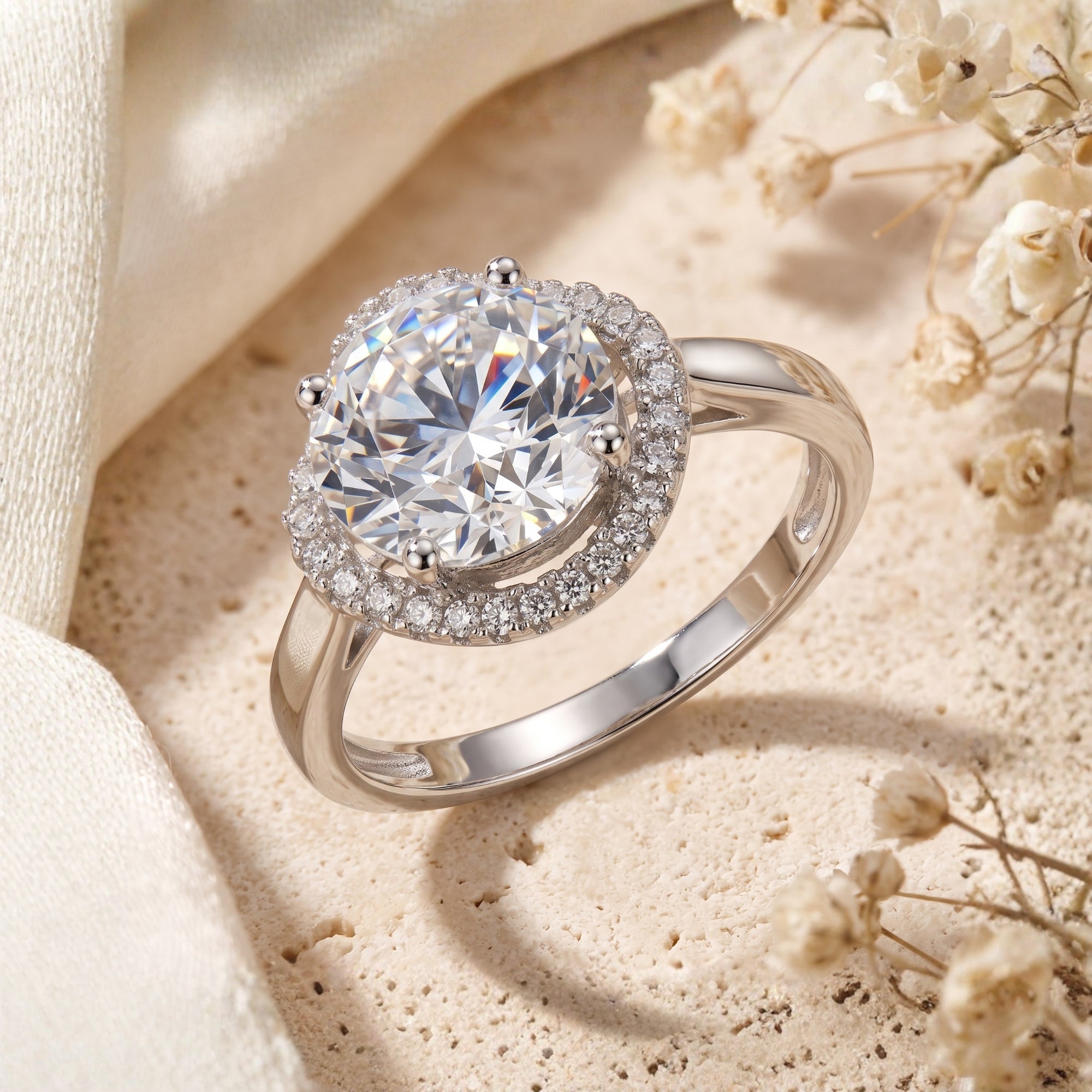 Round halo simulated diamond ring in sterling silver on stone with dried flowers.