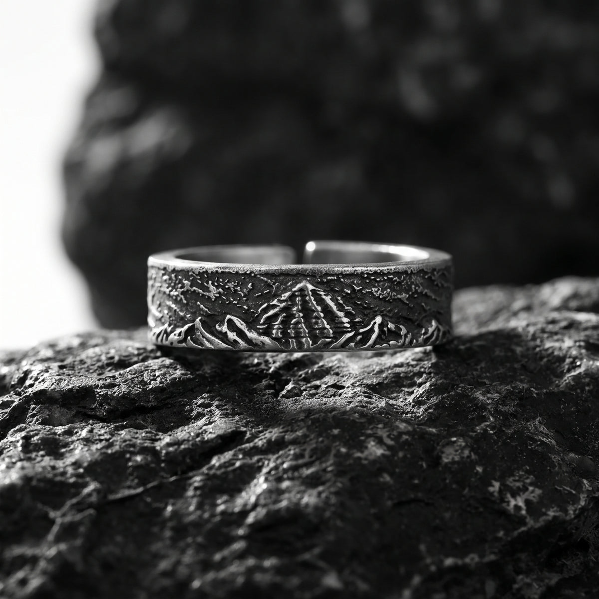 Front view of the silver open-band ring with carved mountain ridge relief resting on dark rock.