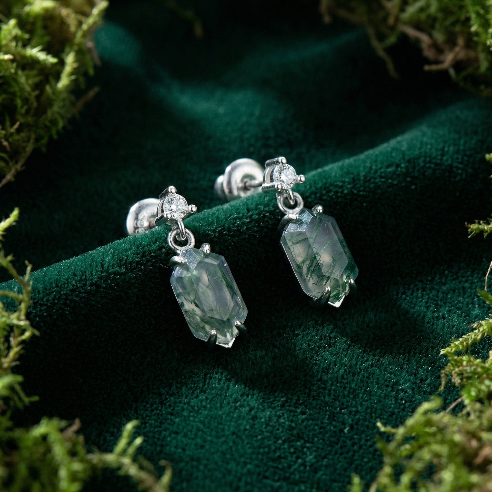 Barrel cut moss agate dangle earrings in S925 sterling silver on green velvet with natural moss accents.