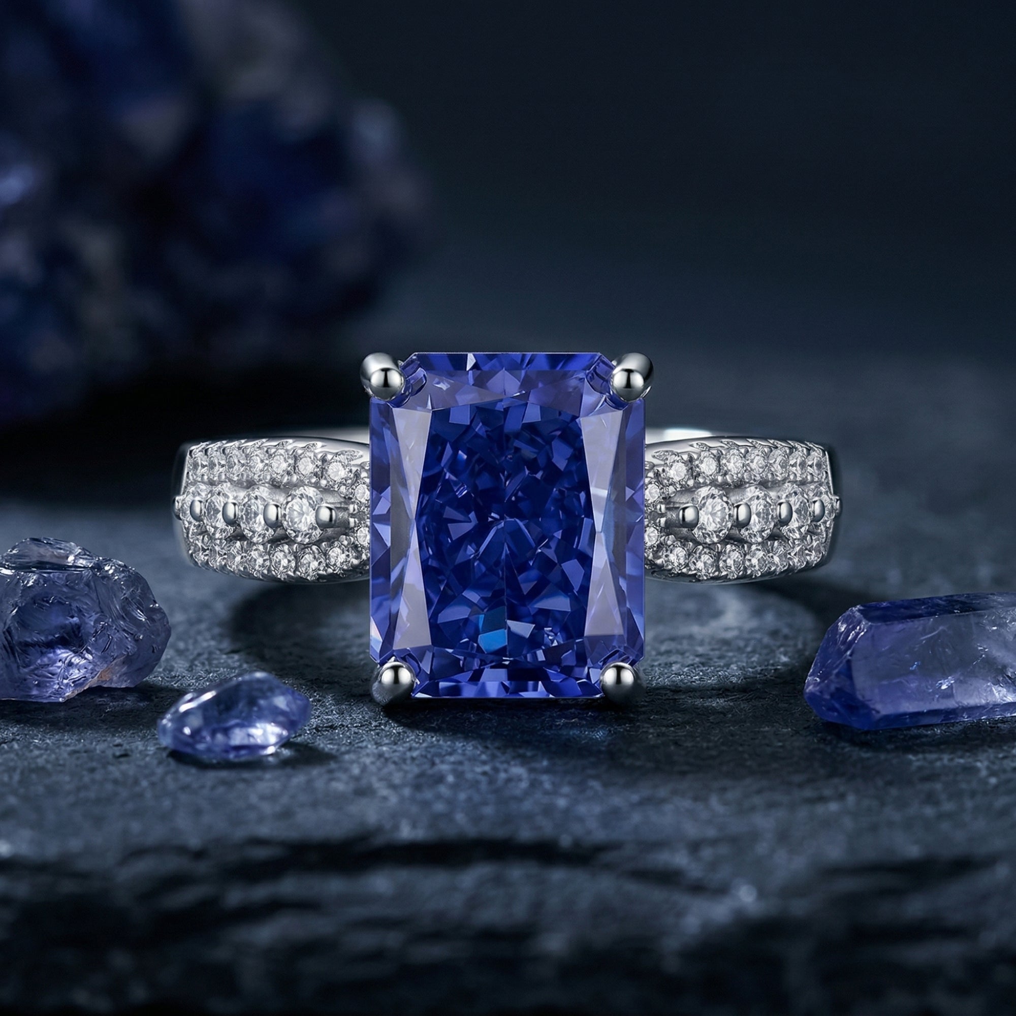 Radiant cut natural tanzanite ring in sterling silver on a dark textured background with raw gemstones.