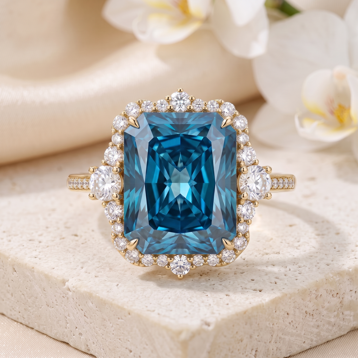 Frontal view of a radiant cut blue moissanite halo ring in yellow gold resting on a stone display block.