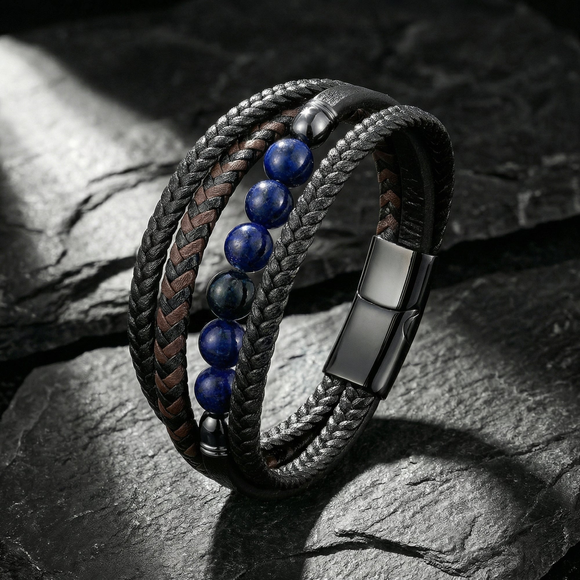 Multi-layered black leather bracelet with blue lapis beads and black stainless steel clasp on a dark stone background.