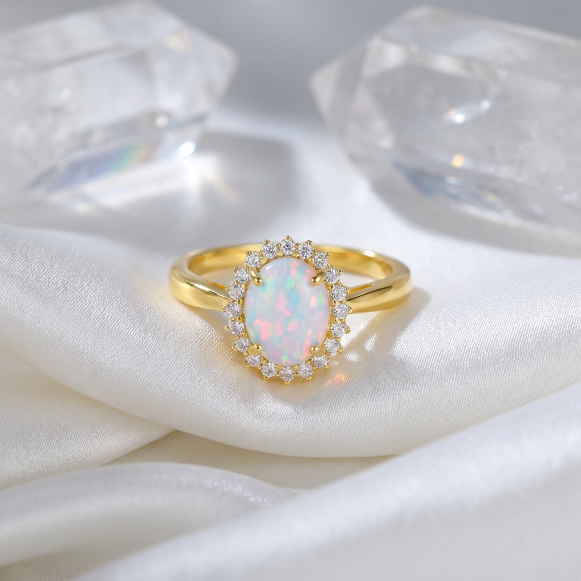 Gold vermeil oval opal halo ring displayed on white silk with decorative quartz crystals.