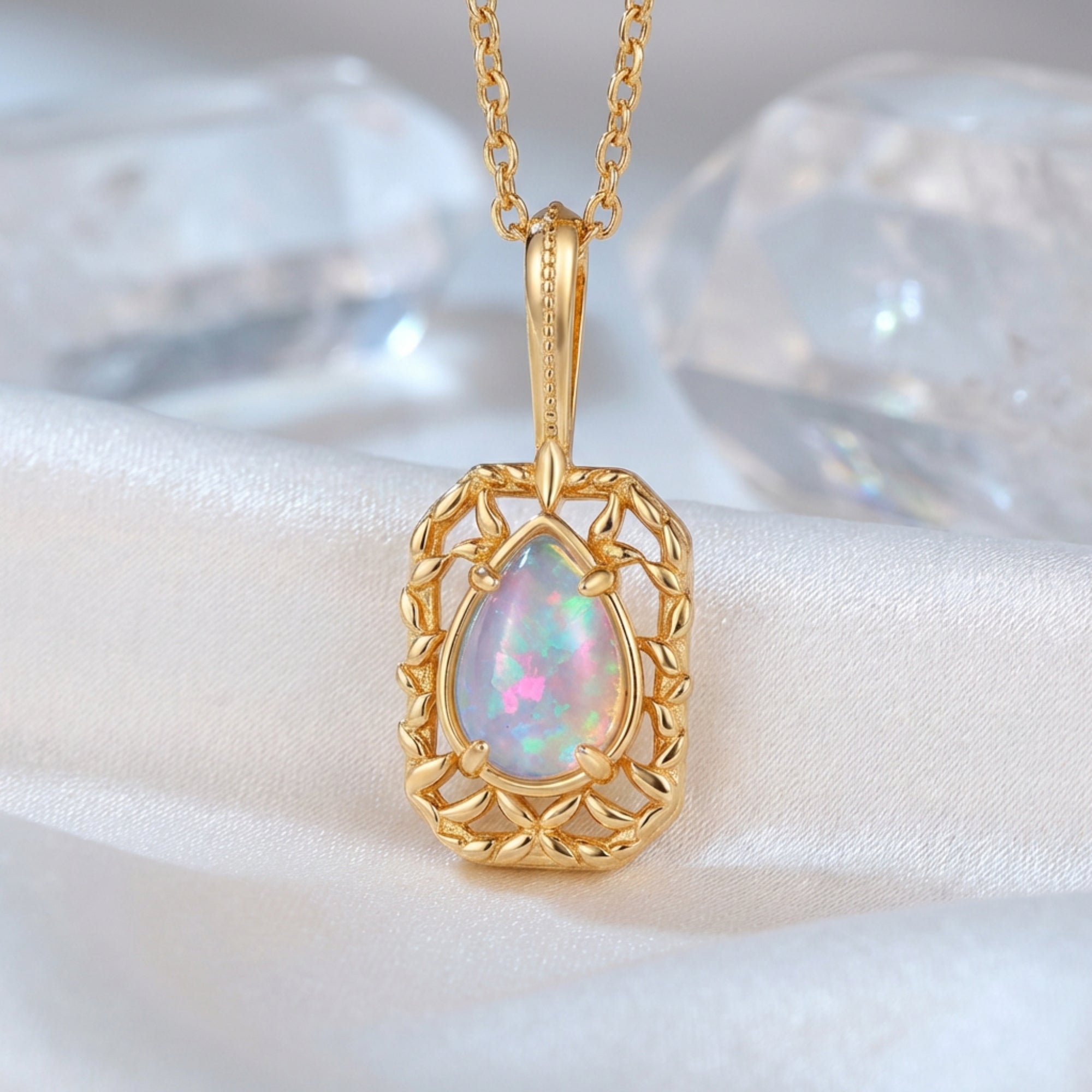 Pear-cut natural opal pendant in a gold-finished filigree frame on white silk with crystal accents.