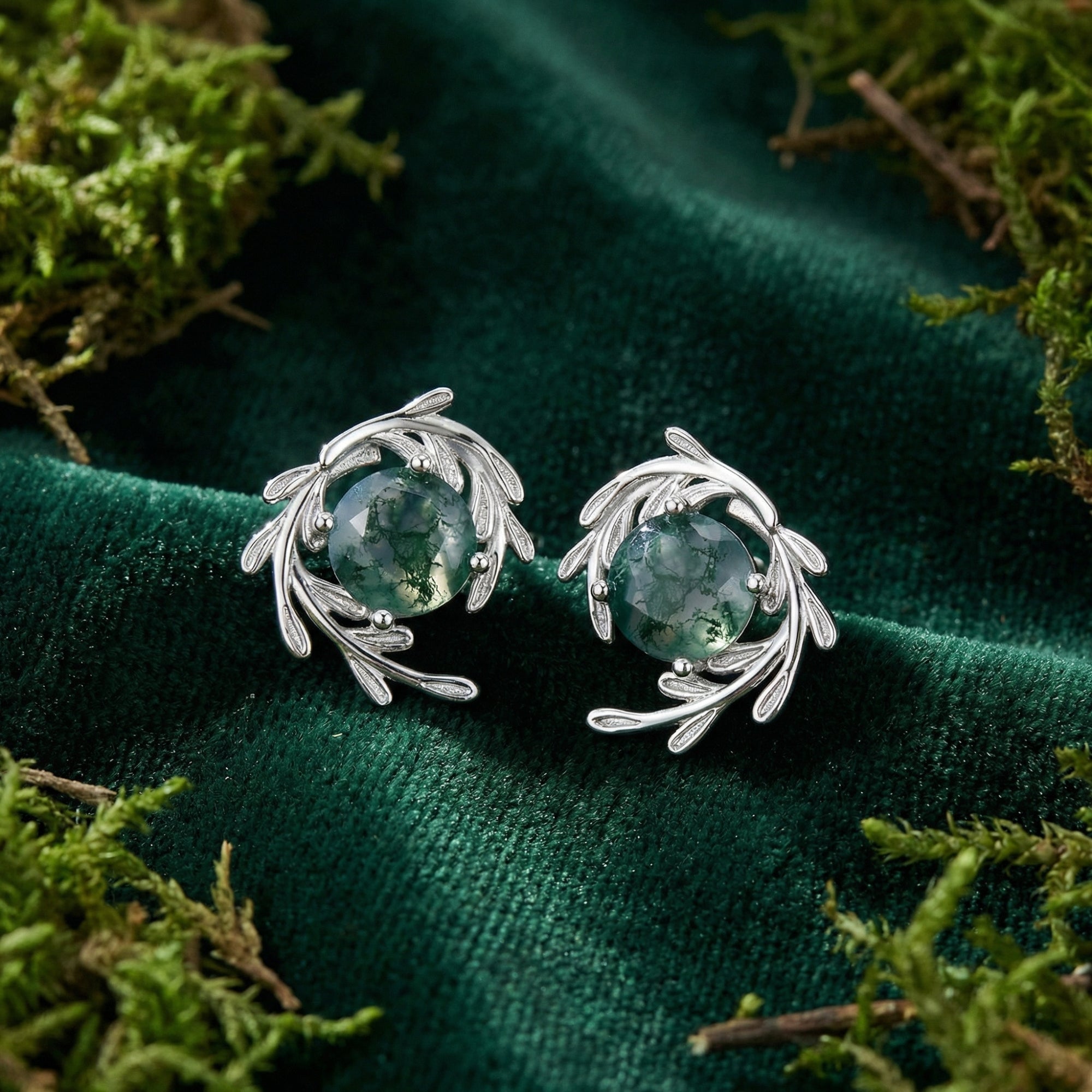 Silver vine wrap stud earrings with round moss agate stones on a green velvet background with natural moss.