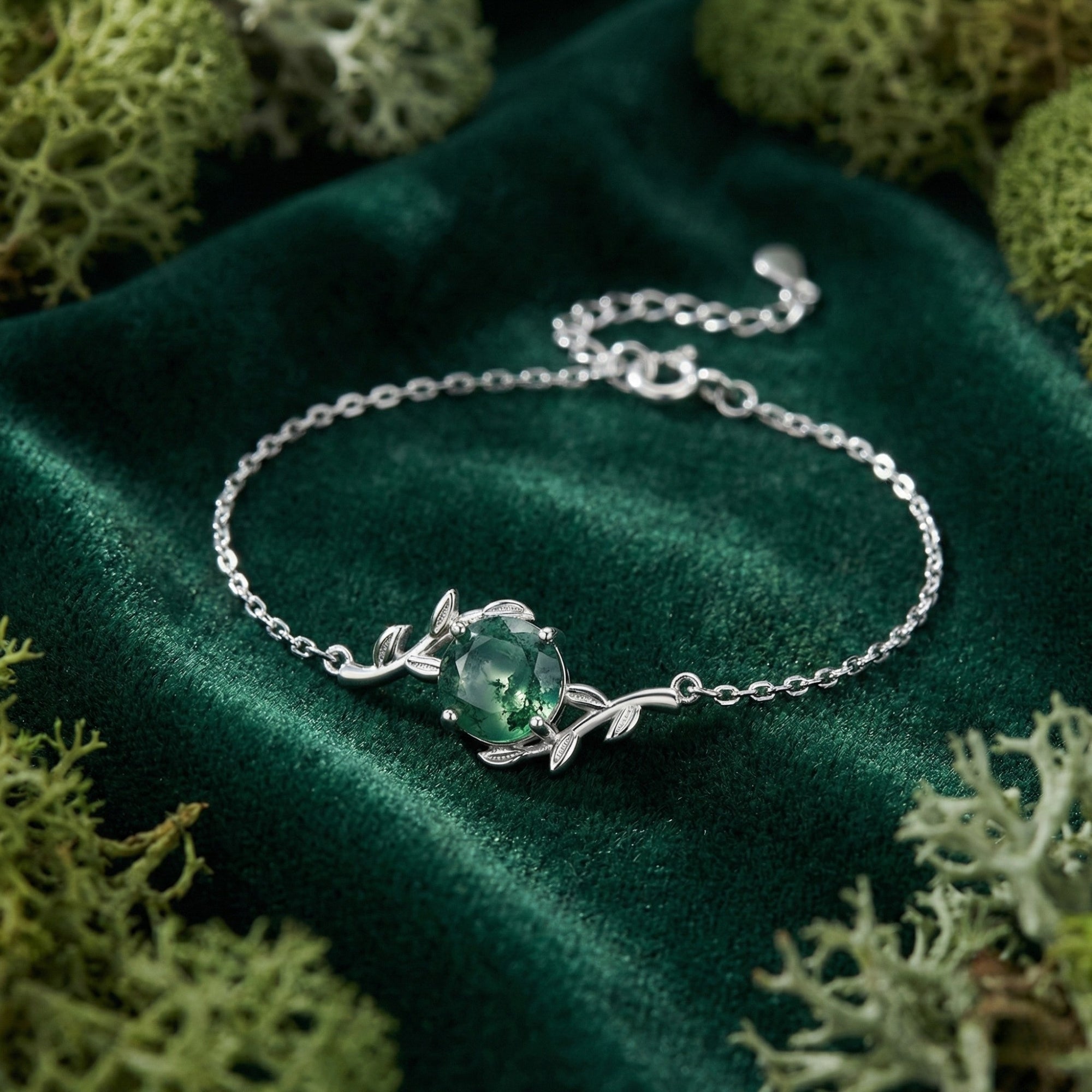 Vine wrap sterling silver bracelet with a round moss agate stone on green velvet and moss background.