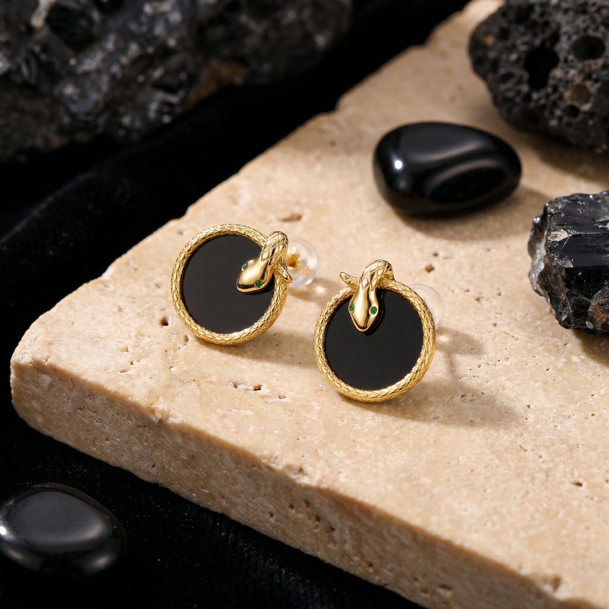 18K gold plated Serpens stud earrings with round black onyx and green eyes on a stone lifestyle background.