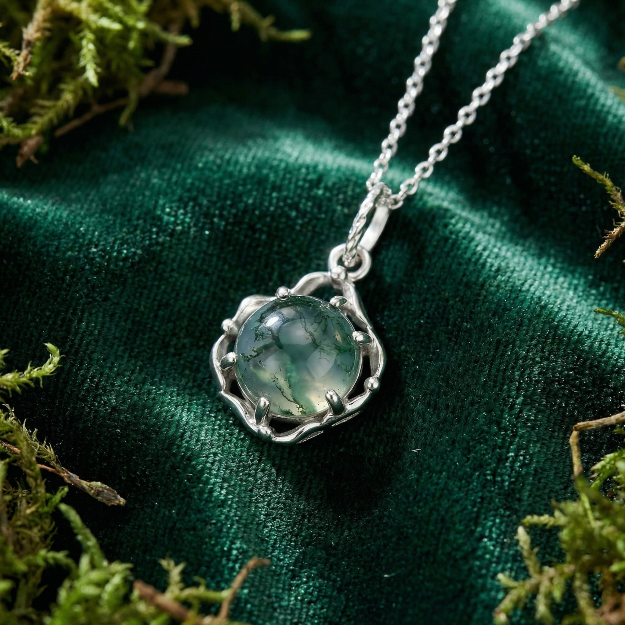 Round cabochon moss agate pendant in a sterling silver celtic knot setting on green velvet with natural moss.