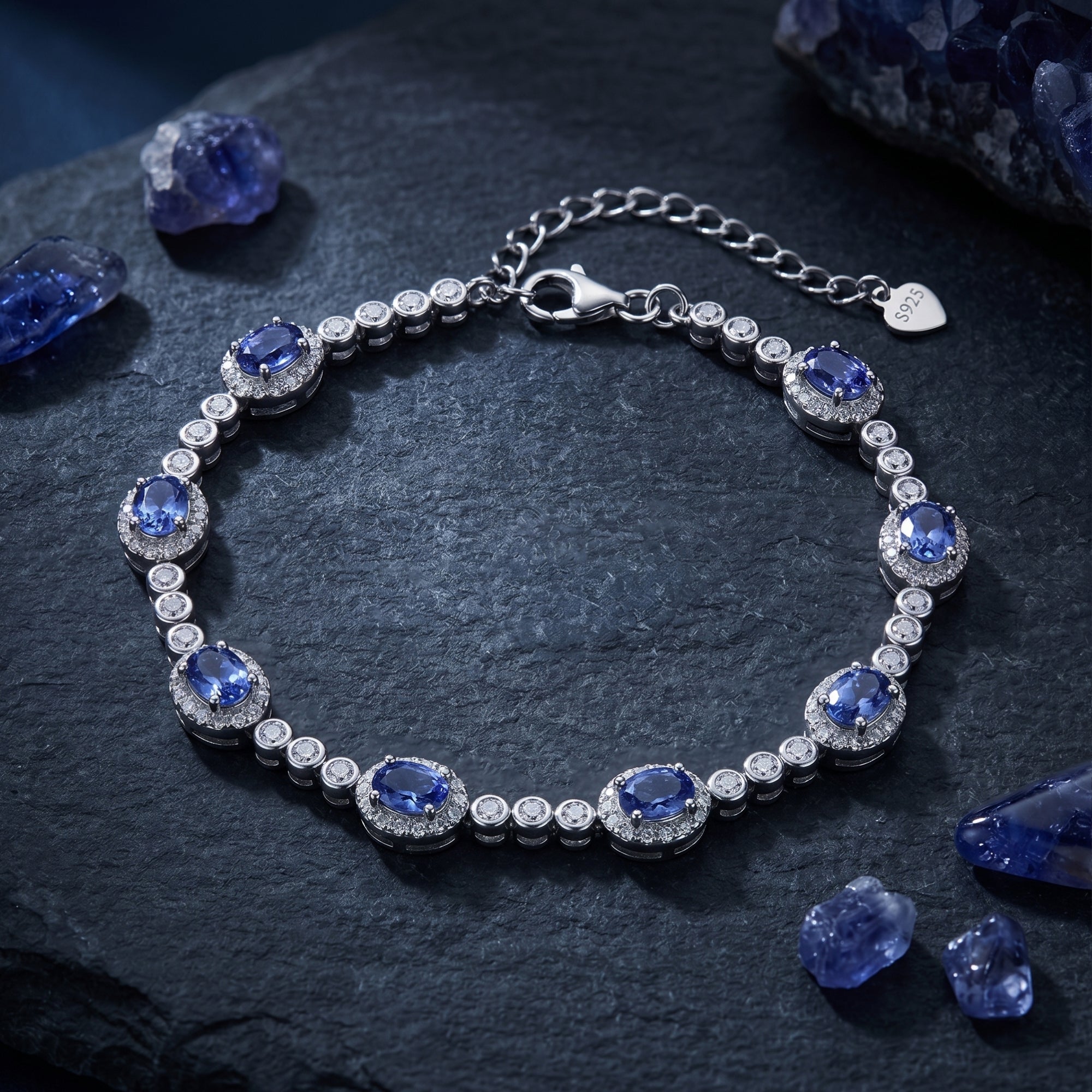 The Xanthe oval cut natural tanzanite line bracelet in sterling silver on a dark stone background with raw gems.
