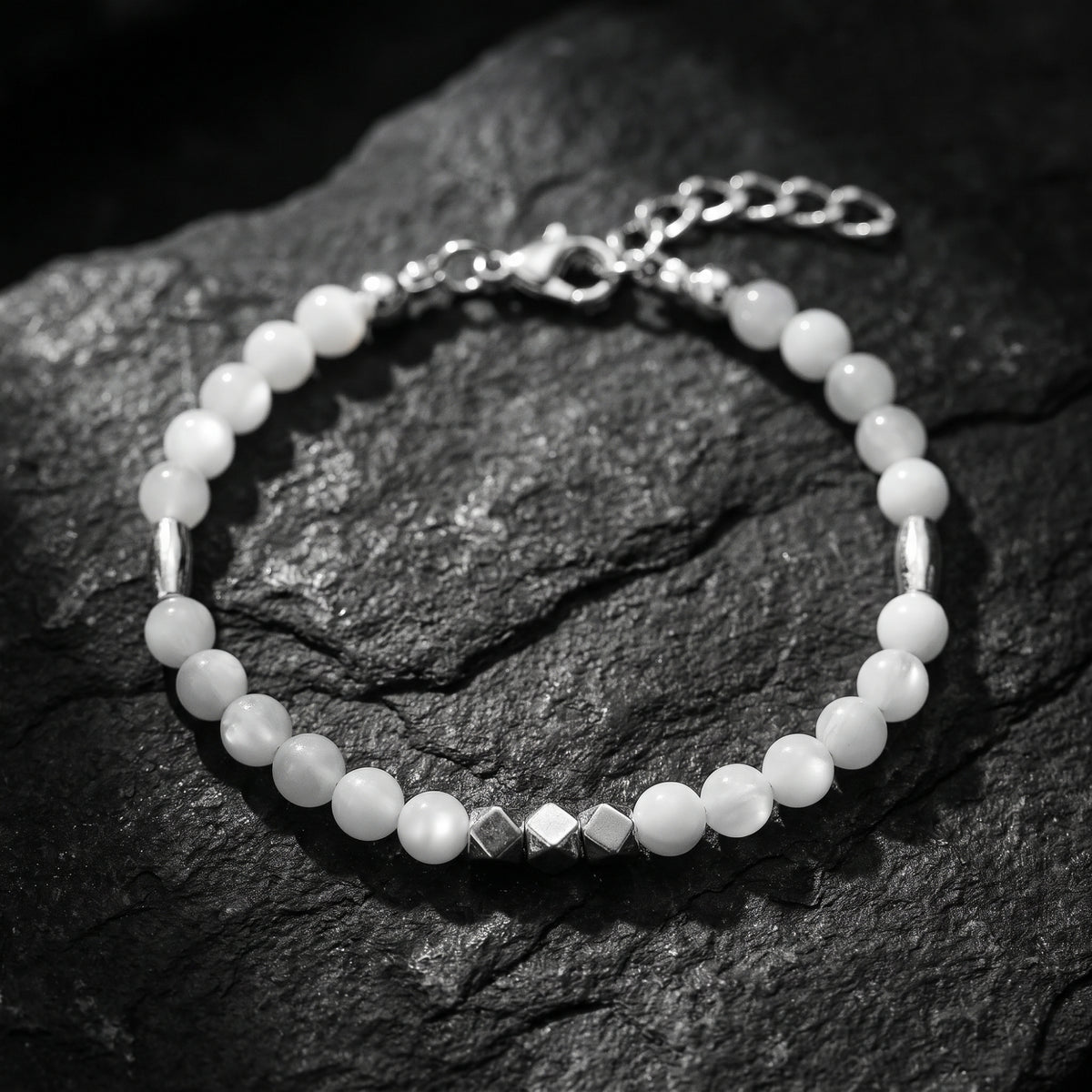 Top-down view of a white beaded bracelet with silver cube accents and an extension chain on dark slate.