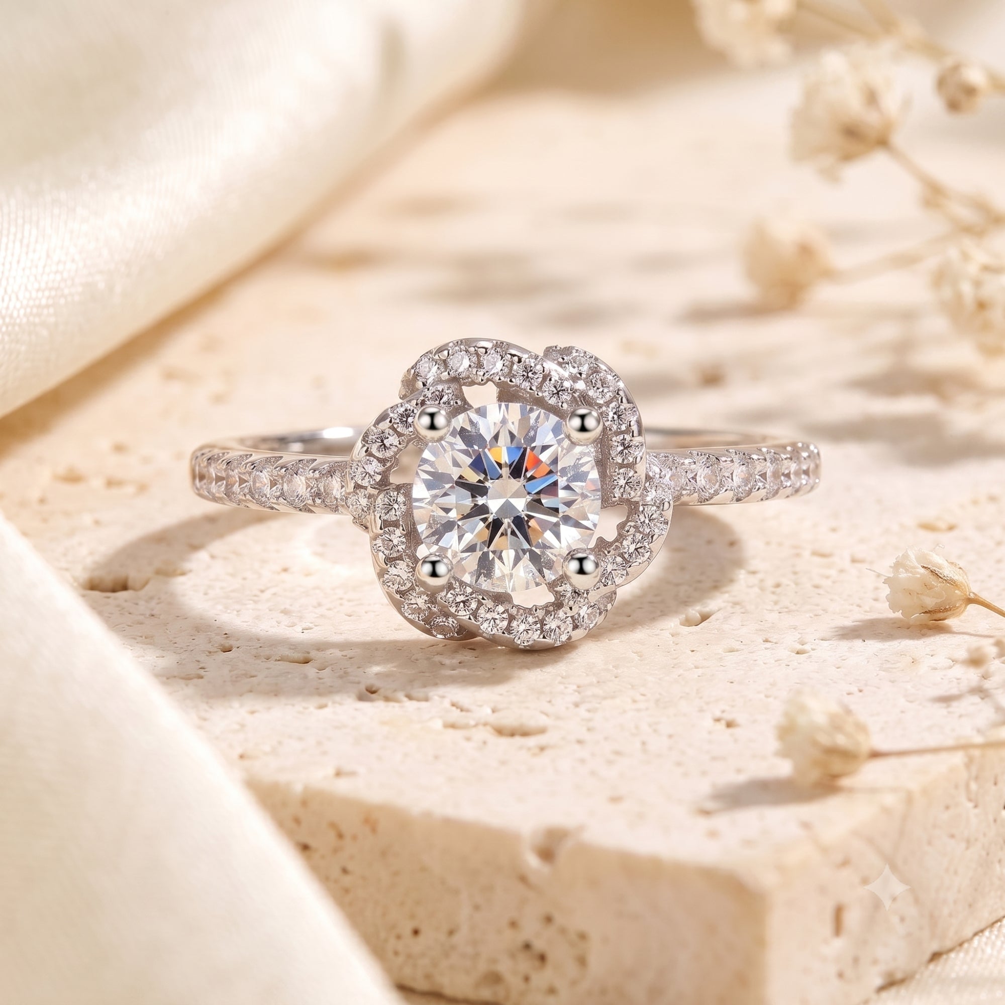 Silver rosette swirl halo ring with round-cut simulated diamond on a stone surface with flowers.