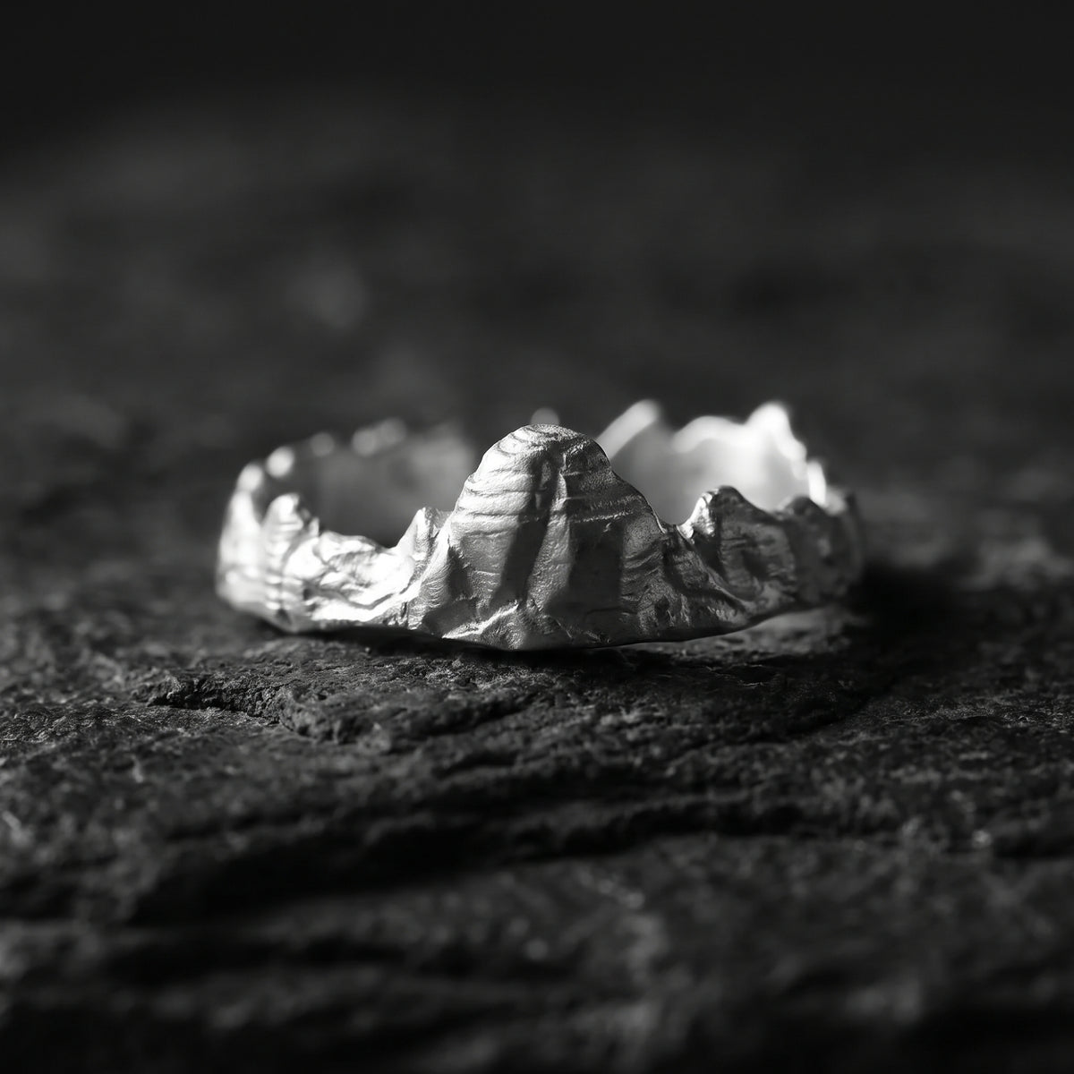 Front view of the silver Summit Ridge ring with a textured mountain ridge profile resting on dark slate.