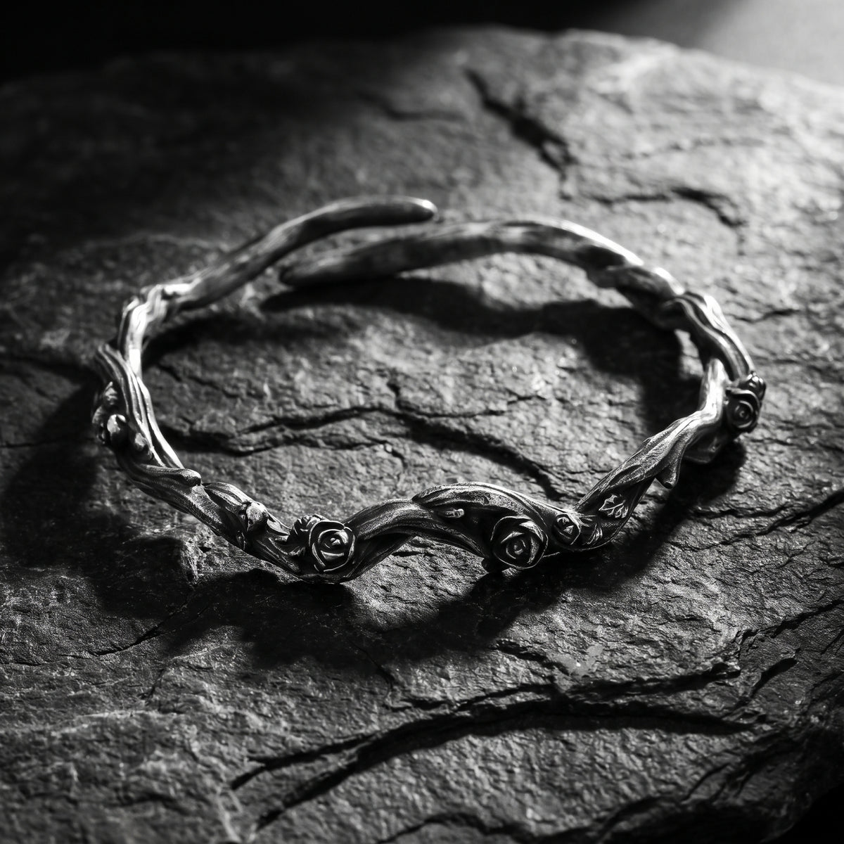 Silver rose vine cuff bracelet with carved rose details, displayed flat on dark slate stone.