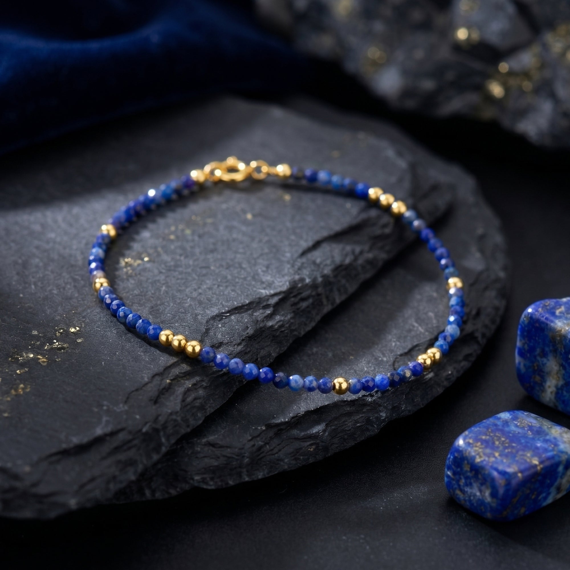Celestial Dawn lapis lazuli bead bracelet with 18K gold plated accents styled on a dark slate rock.