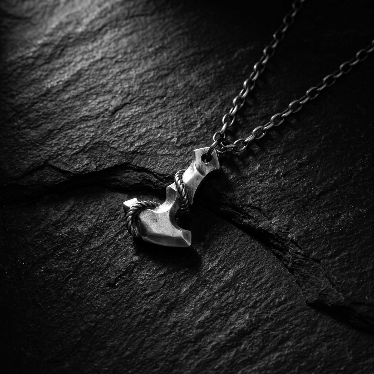 Silver Mjolnir hammer pendant with rope detail resting on dark textured slate.