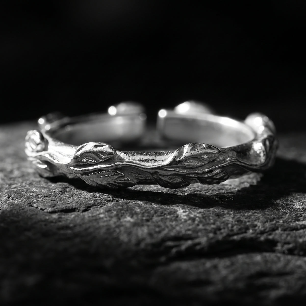 Close-up macro of the silver open-band ring with detailed carved leaf patterns resting on a dark stone.
