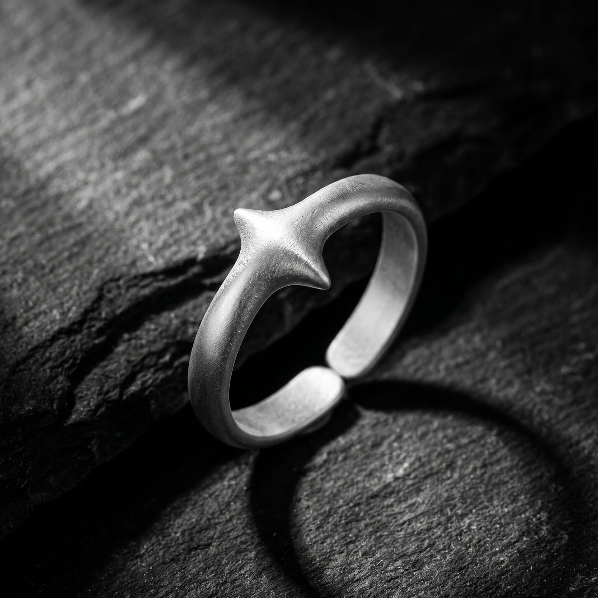 Matte silver open band ring with a raised four-point star, standing on a dark slate surface.