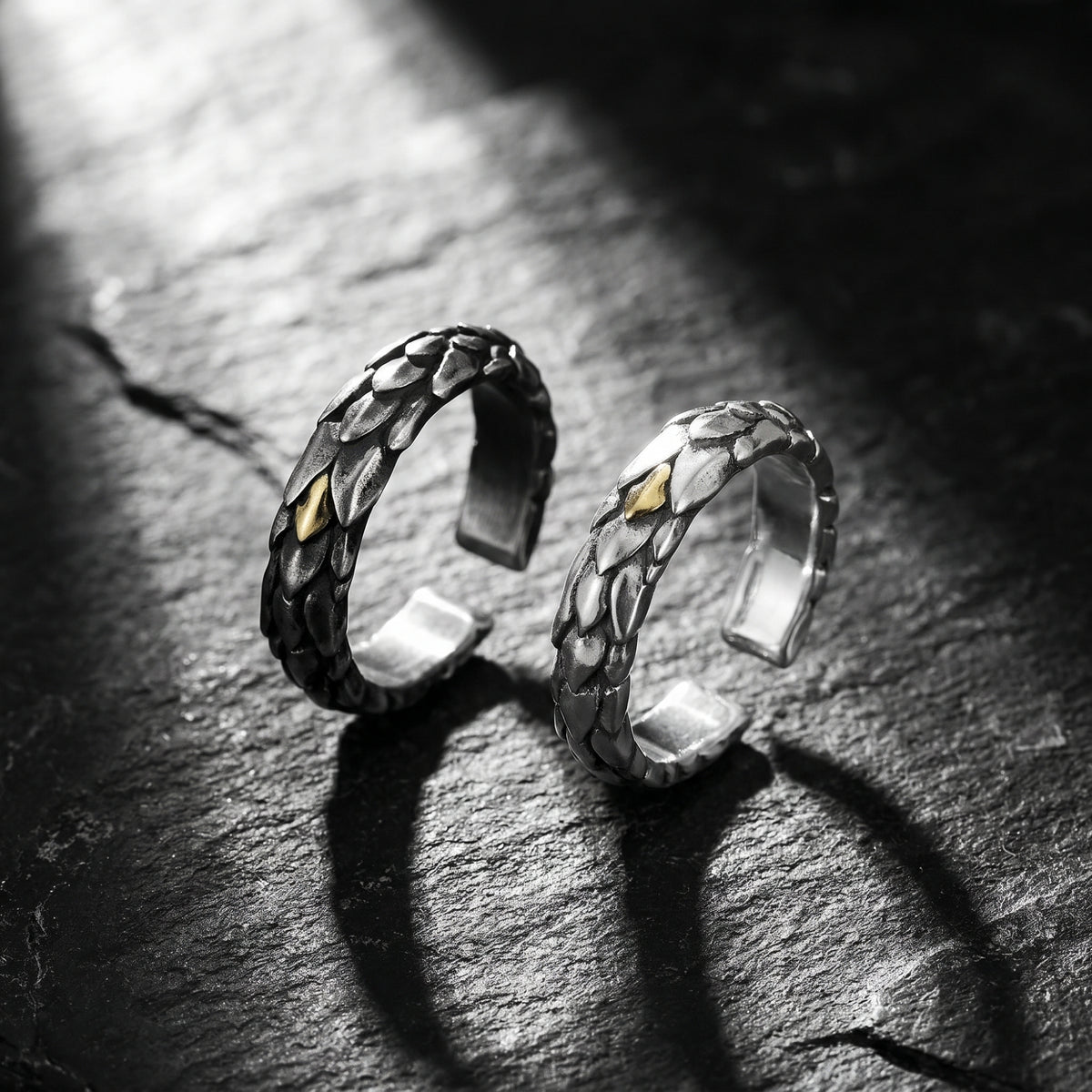 Two open rings with dragon-scale texture and gold-colored accents, standing upright on dark slate.