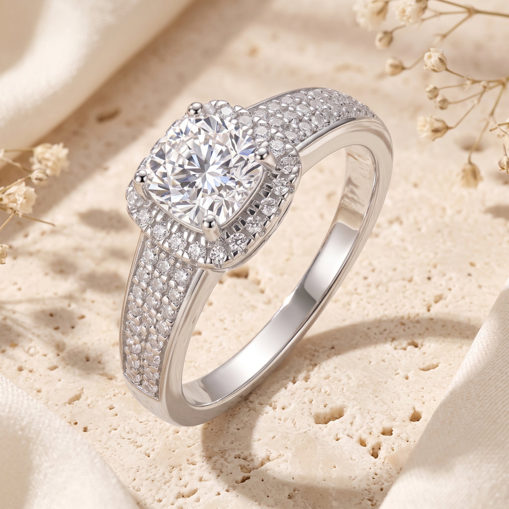 Silver cushion halo ring with pavé band on stone background.