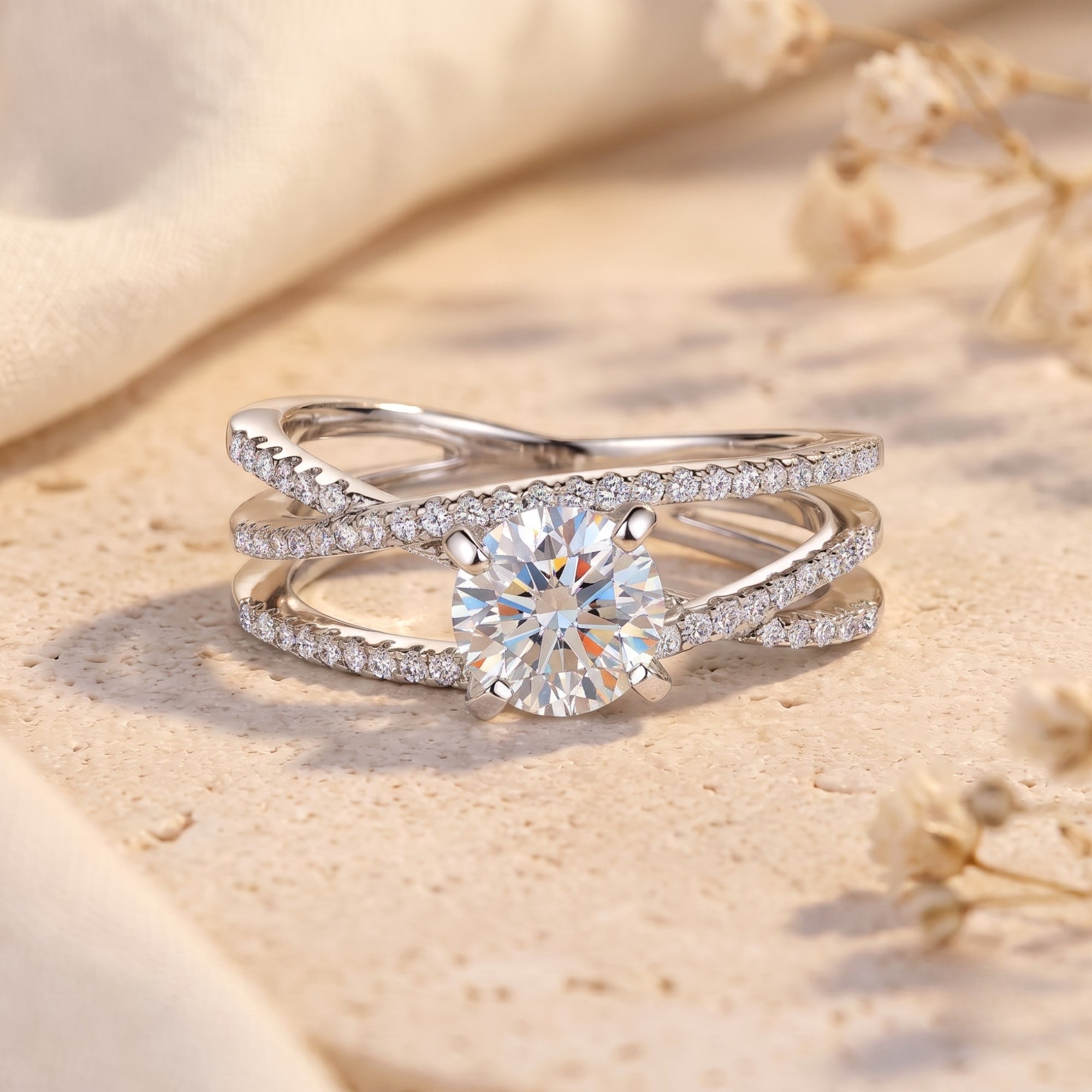 Silver criss-cross promise ring with round center stone on a textured surface with floral accents.