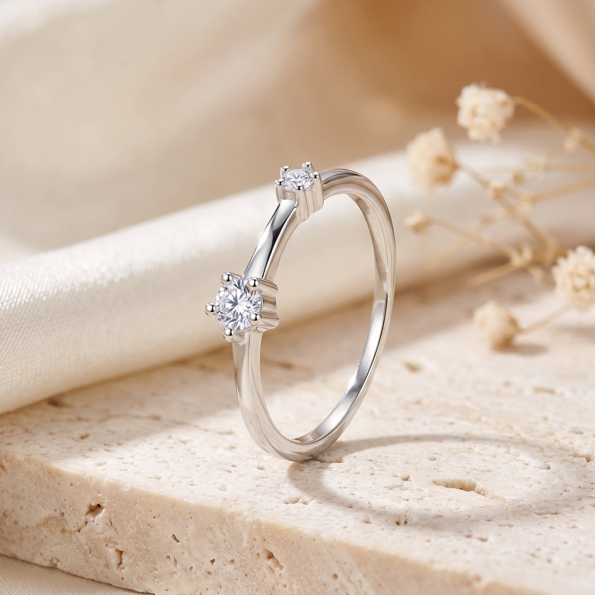 Asymmetric S925 silver bypass ring with two round simulated diamonds on a stone surface.