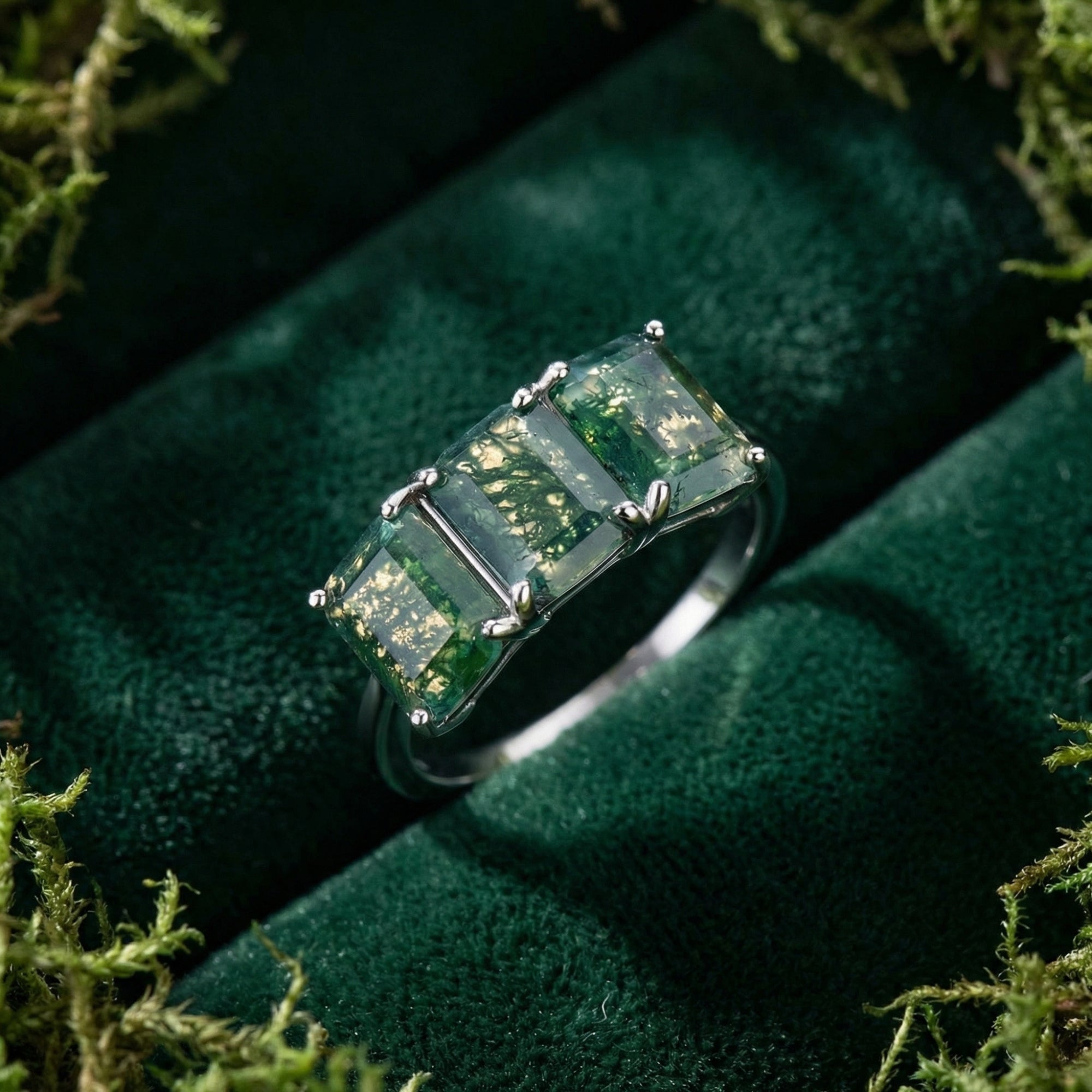 Triple bar cut moss agate stones in a sterling silver ring setting on green velvet surrounded by moss.
