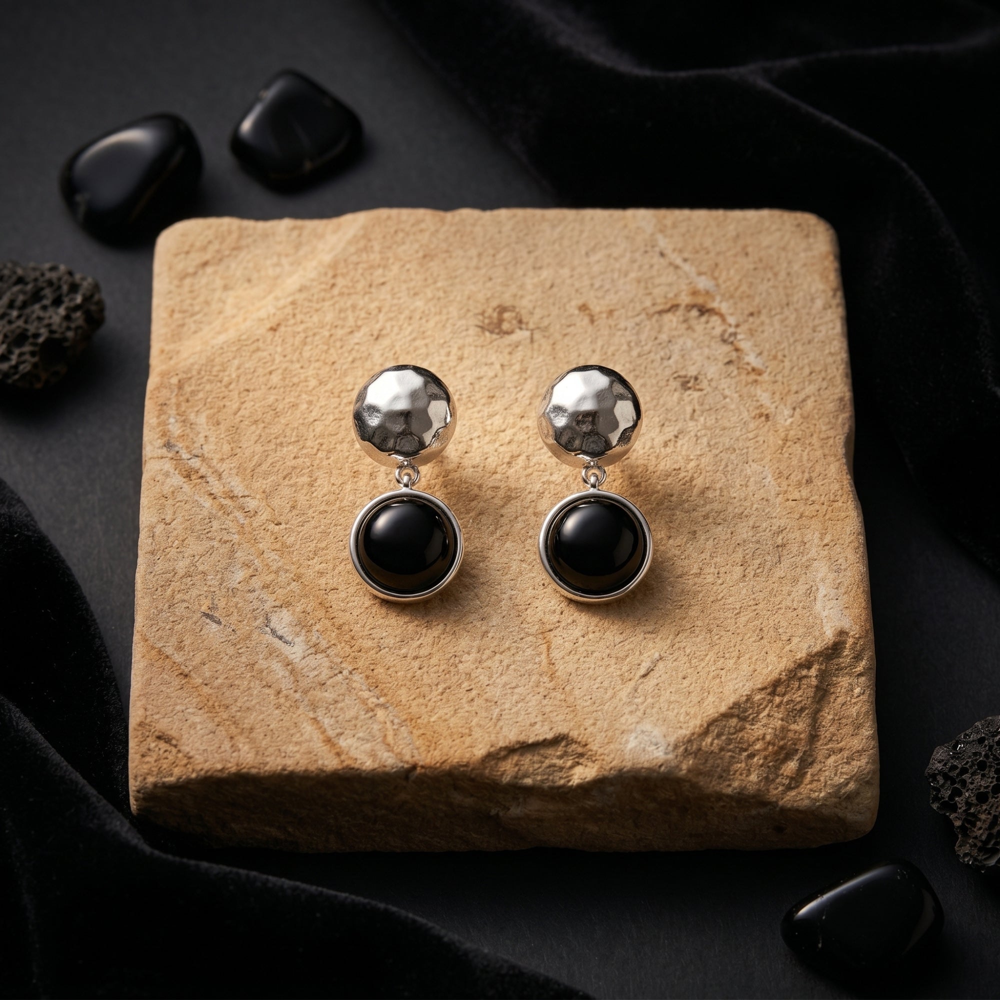 Sereia silver drop earrings with hammered texture and round black onyx stones on a tan stone display.