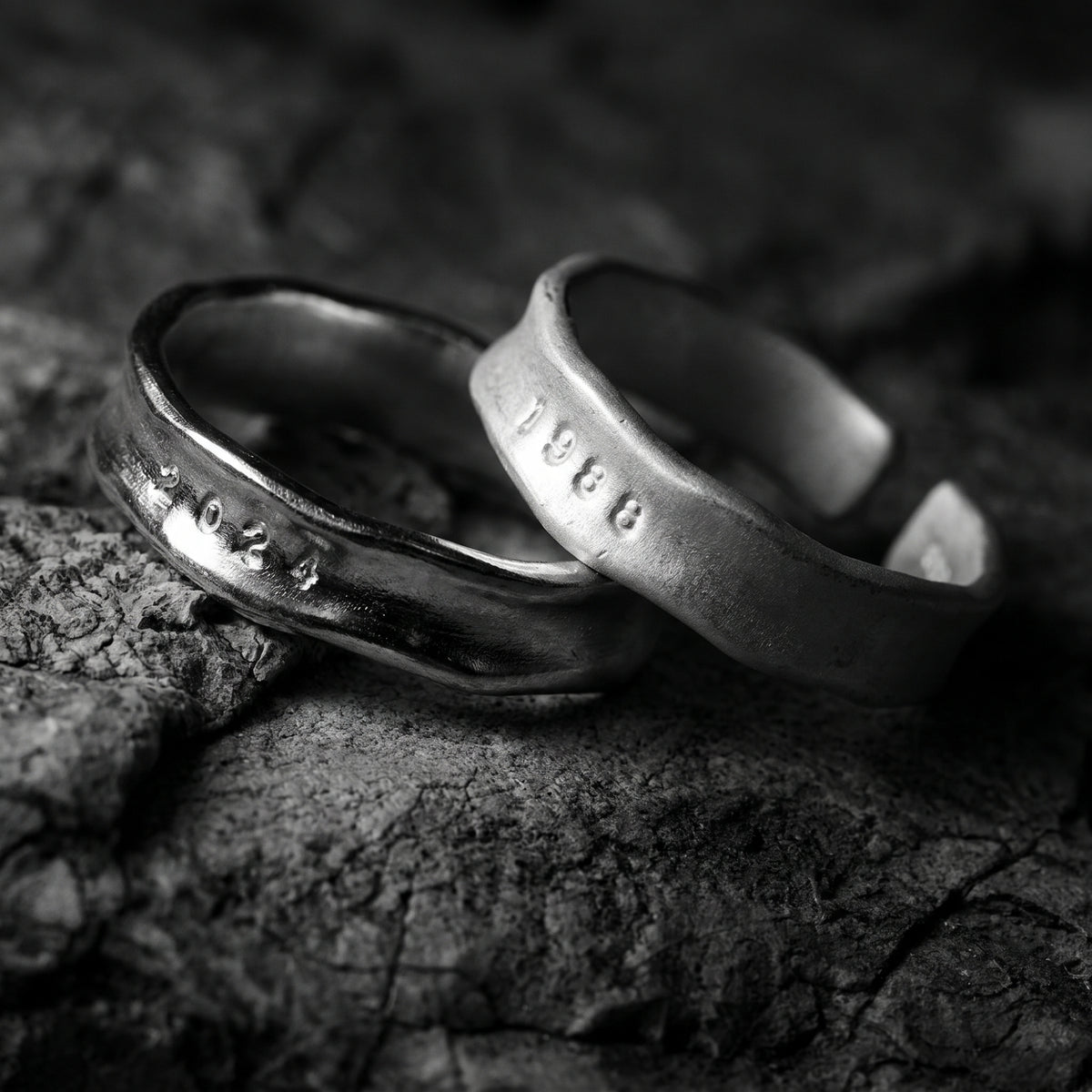 Black-and-white close-up of two textured open-band rings stamped 2024 and 1988 on rough stone