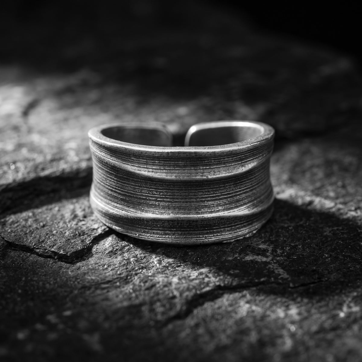 Front view of a silver open-band ring with a concave ribbed surface, displayed on dark slate.